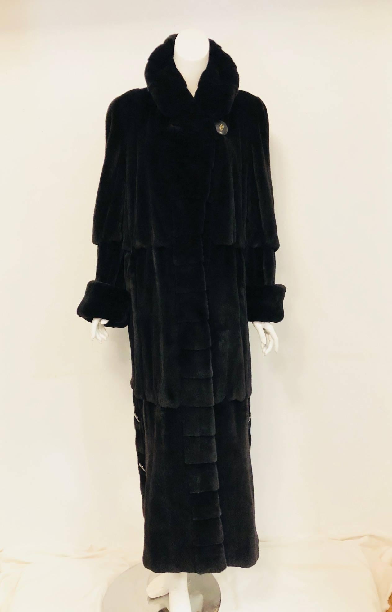 Marshall Fields luxurious  black sheared mink coat with 3 tier bands of vertical pelts creates a ruffle effect.  This coat has a slit at each side at the bottom of the coat with 2 acrylic and brass decorated buttons for closure.  The round collar
