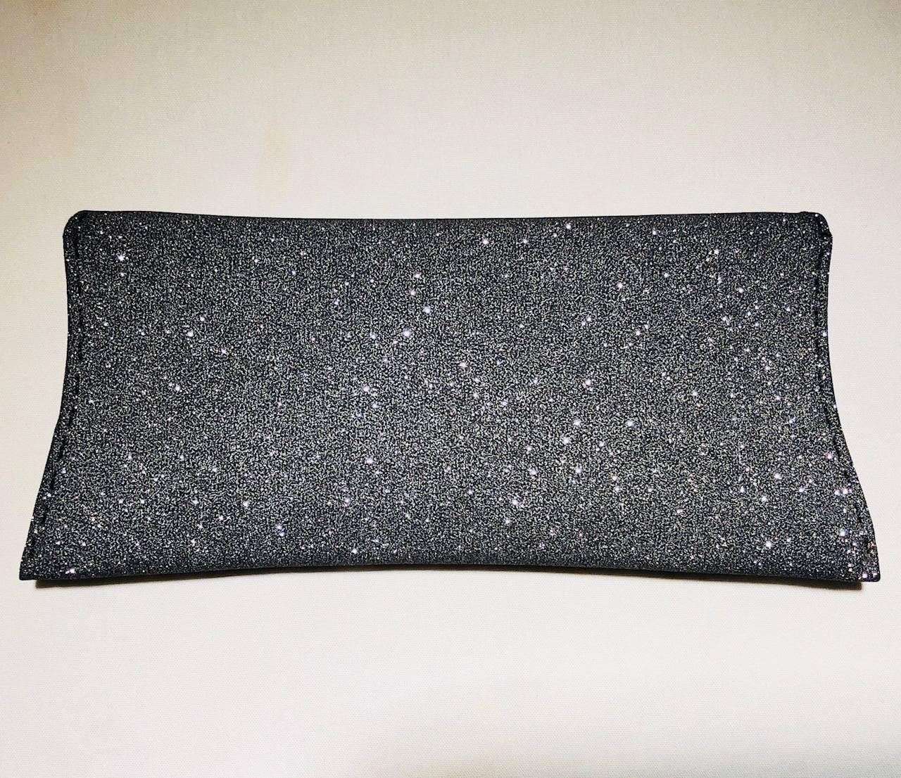 VBH  dark silver sparkle Manila clutch with overlay push through closure.  The interior is lined in grey suede with one small slit pocket.  Pick stitch detailing can be found around the bag in black thread.  Three metal studs at front closure.  In