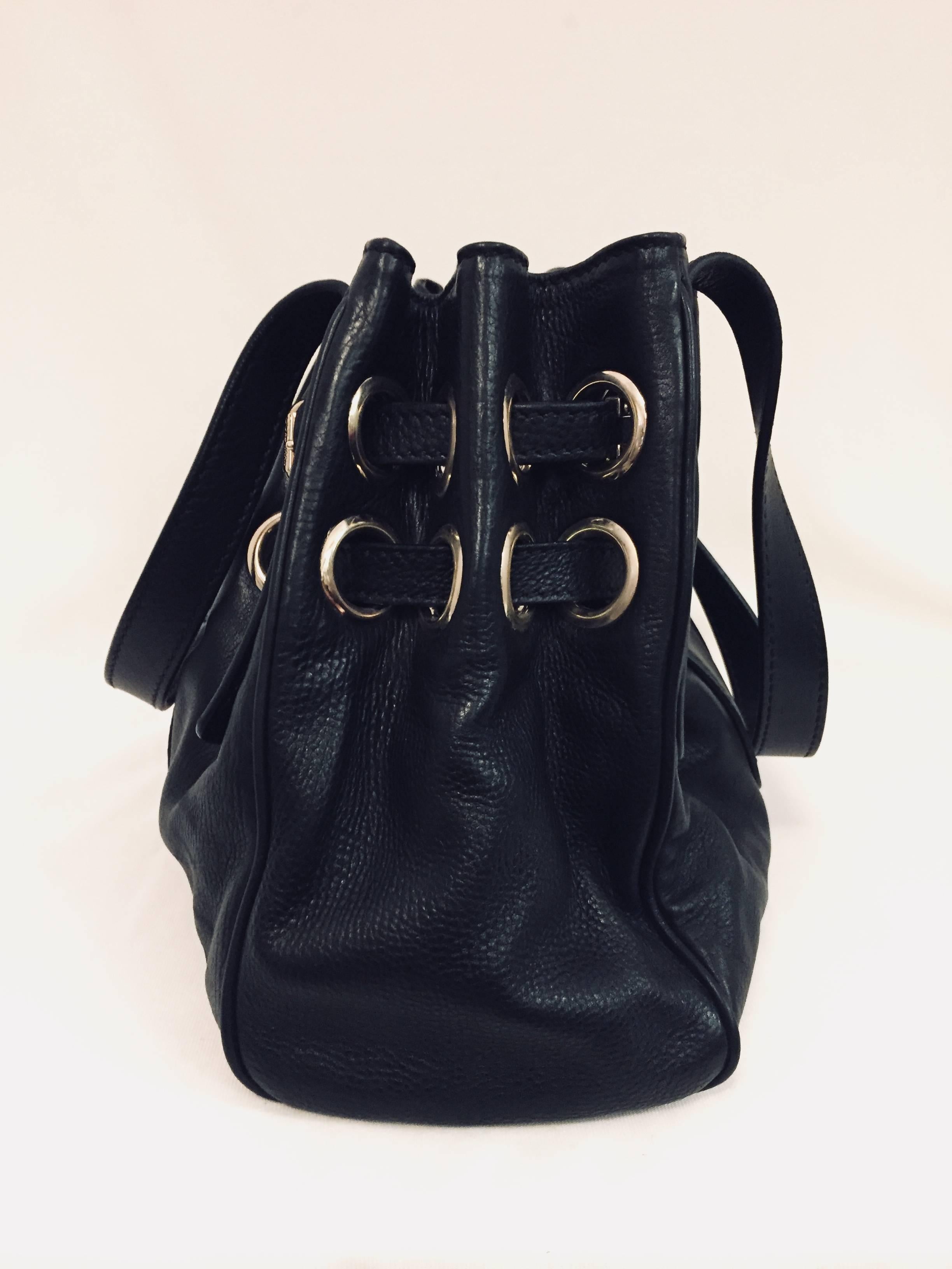 Jimmy Choo Black Shoulder Bag is crafted from luxurious black grained leather and features gold tone hardware, buckle detail threaded through large grommets, double flat handles and small flap with logo engraved flip-lock closure.  Signature gold