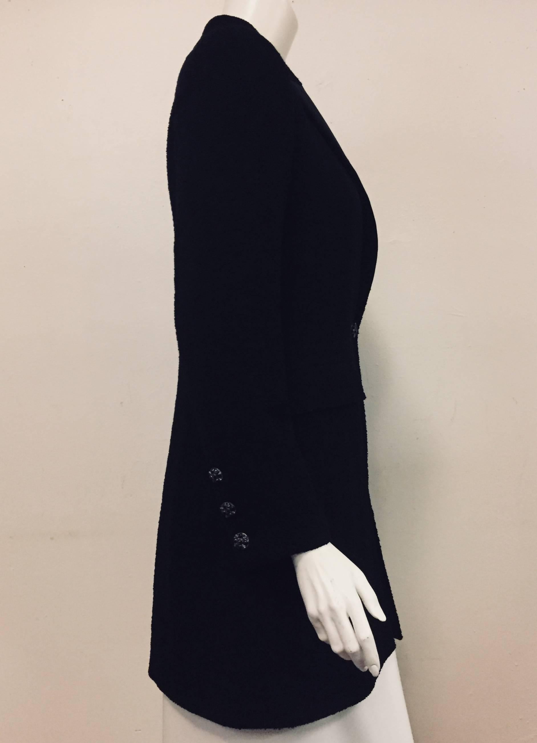 This Chanel black wool blend tuxedo style long jacket incorporates a notch collar with a satin lapel.  For closure two pewter tone metal buttons with inlaid black stones are hanging from a chain on each side of front closure.    Four of the same