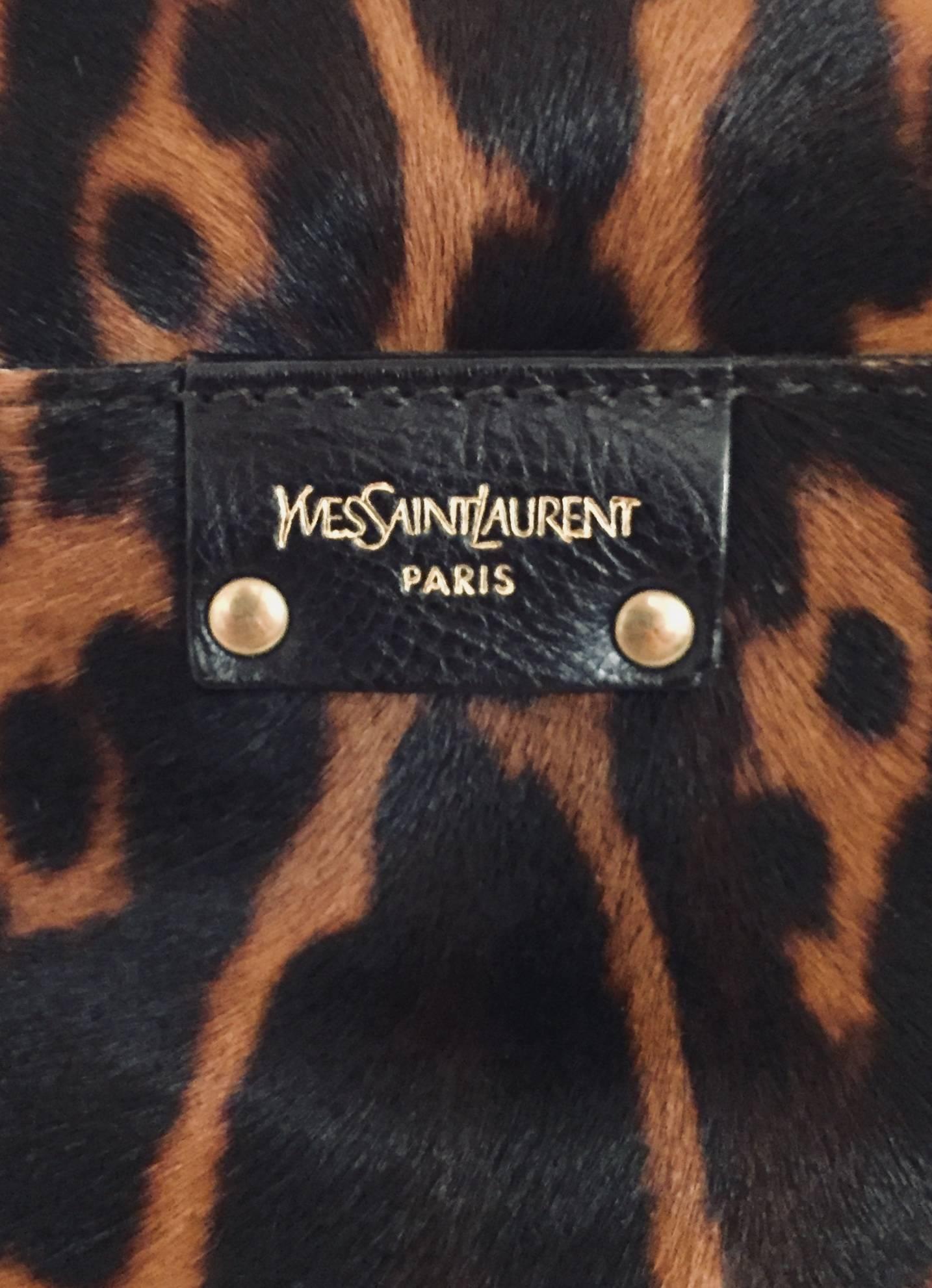 Exceptional Yves Saint Laurent pony hair leather printed as leopard skin has two brown leather handles and large flap with 2 wooden charms at closure.  All around the flap you will discover brass colored studs, as well as on the strap.  The inside