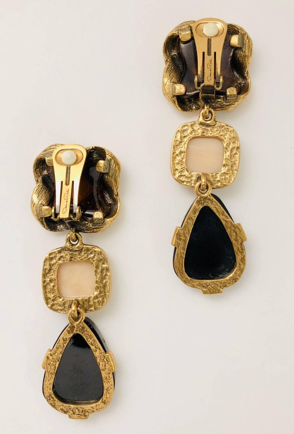 Oh, Oscar!  These fantastic gold tone dangle earrings are a statement!  Three distinct stations begin with smokey brown resin covered with a hammered, intertwined design, followed by gold tone framed ivory resin and ending with painted jasper resin