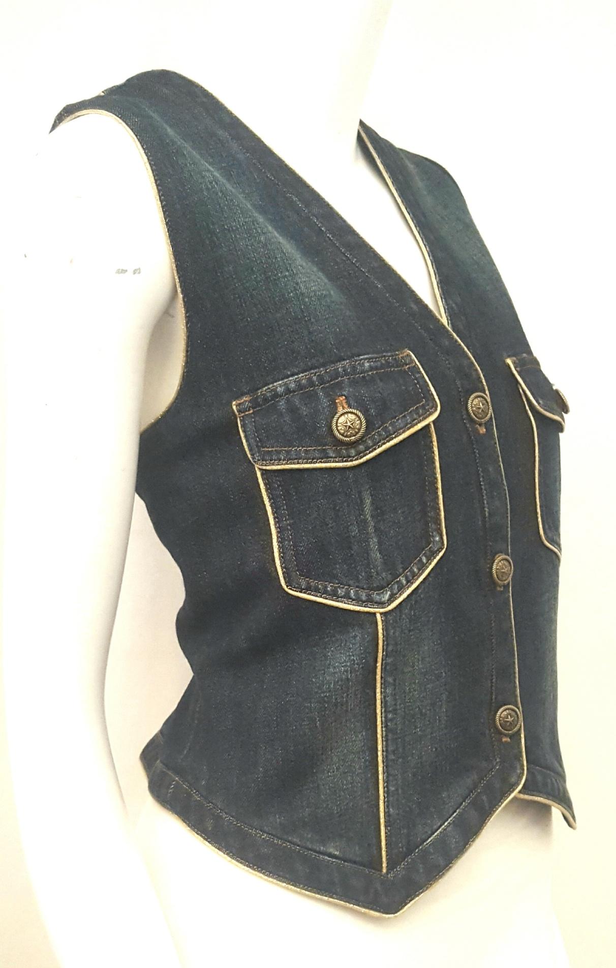 Chanel denim vest with gold tone cord trim all around both at front and back provides a glamorous accent to this casual garment.   This V neck vest has a pointed hem at the front and two flap pockets with brass buttons on flap.   For closure this