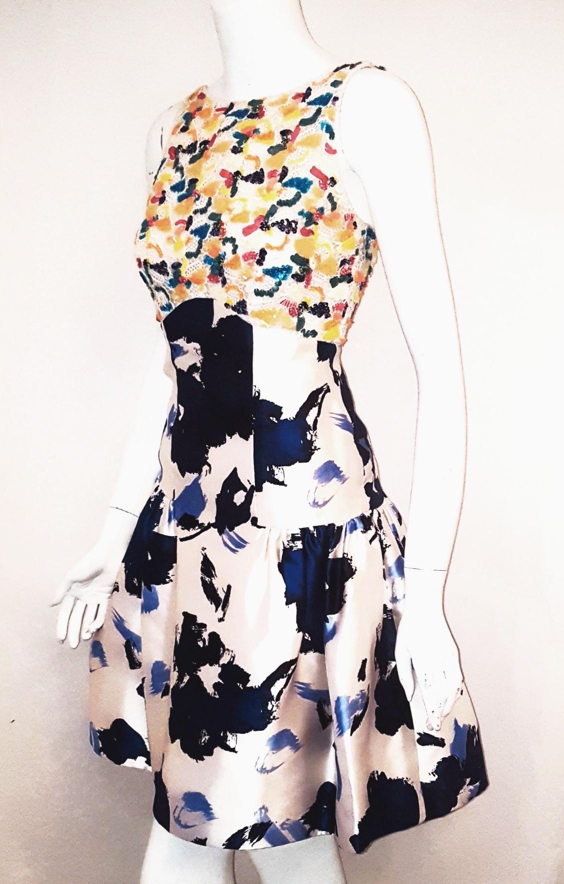 Oscar de la Renta's mix media white and royal blue silk dress is detailed with multi color sequins in a whimsical design on white cotton lace.  The dress is cut to a fit and flare silhouette with a pleated skirt.  This sleeveless dress with thin