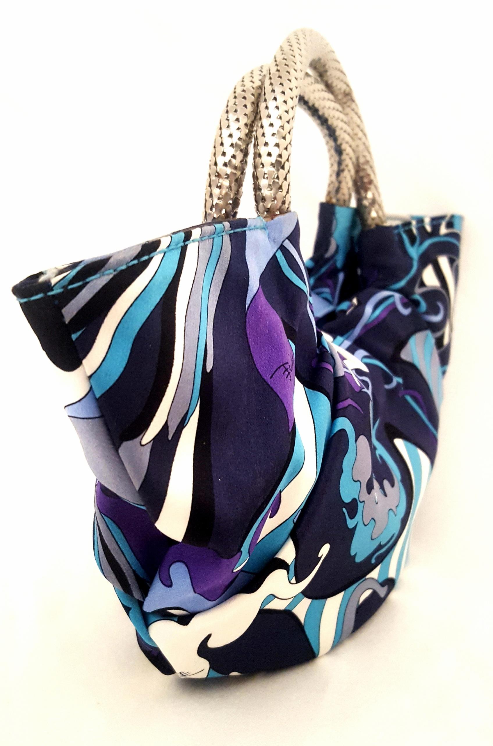Emilio Pucci was a master of abstract, colorful prints.  Flawlessly crafted in Italy and decorated with a signature floral silk print in blue and purple hues, this bag features woven metal two bracelet handles and is finished with a fabric loop