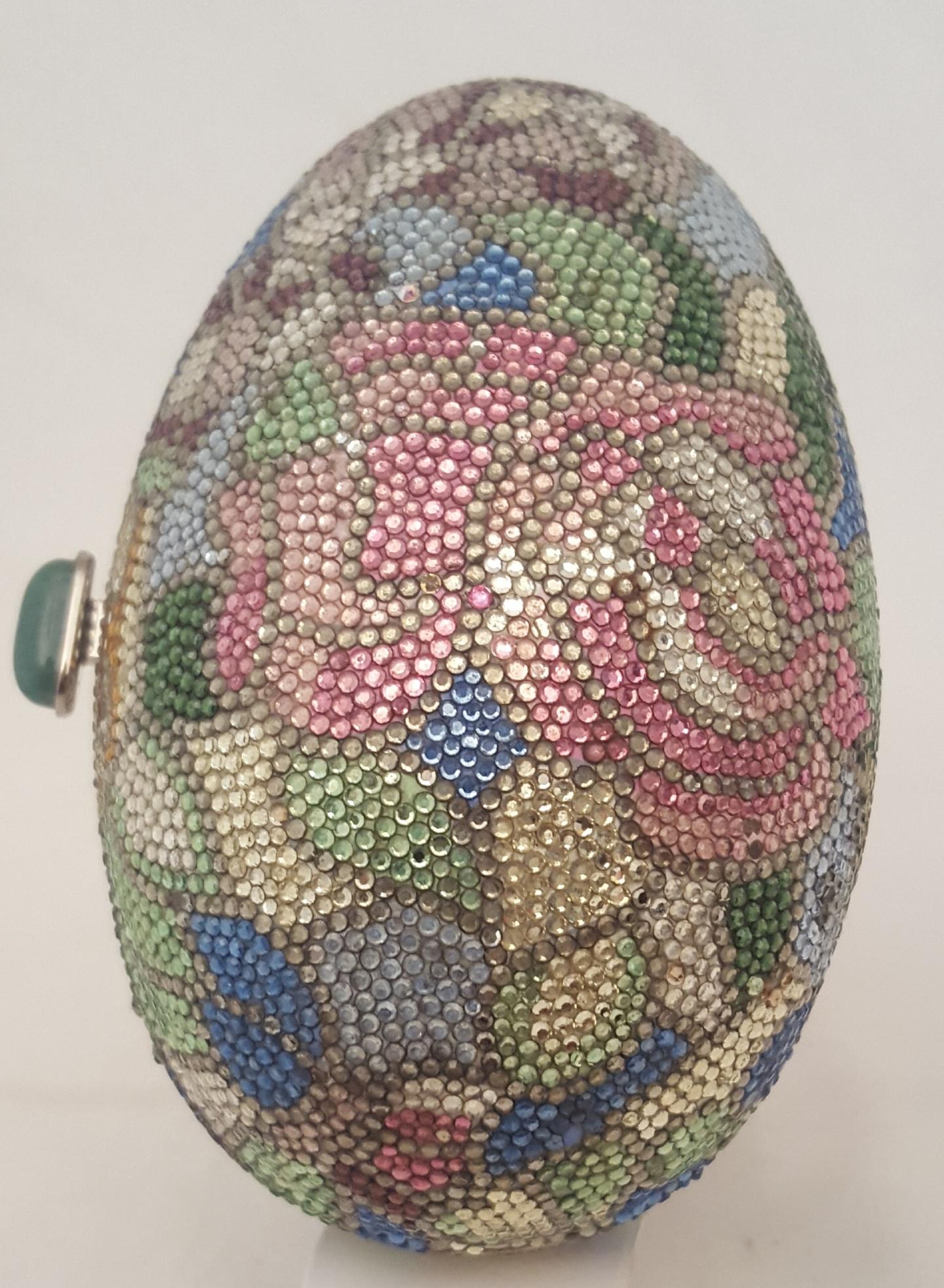 Add to your collection this highly sought after Judith Leiber Egg with Swarovski crystal minaudiere bag crafted from individually placed multi color crystals. This egg with a floral theme contains pink, lavender and white flower on a mosaic