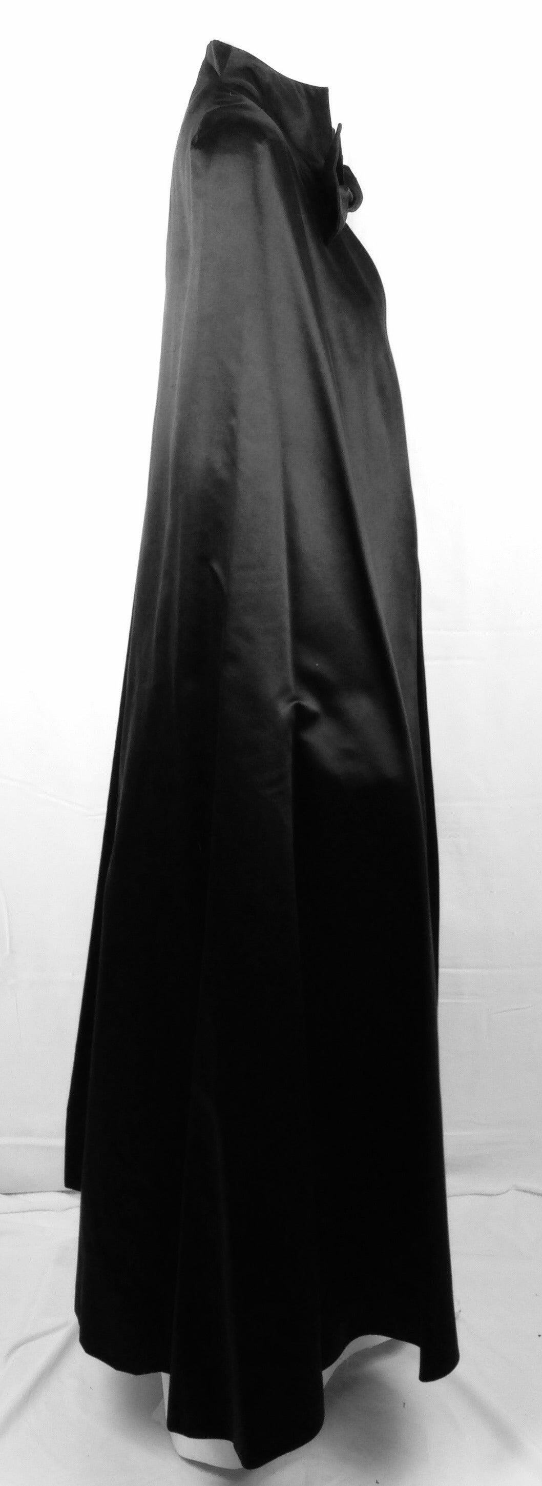 Embrace your inner phantom and make an unforgettable entrance in this stunning long black satin cape by famed designer Pauline Trigere.  Trigere's French background and training are evident in this deceptively simple design.    Self-tying,