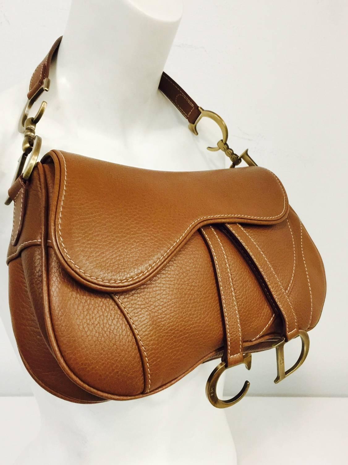 Christian Dior Double Saddle Bag has become one of the most recognizable shapes and highly coveted designs by fashionable women around the world!  Features supple grained leather exterior, looping shoulder strap and hanging straps each with gold