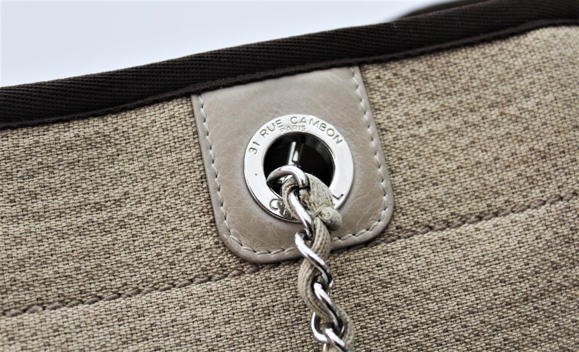 The Chanel Brown Canvas Deauville Small Tote Bag features a durable dark brown canvas body with the traditional Chanel logo stitched in white on the front. The bag comes with chain and fabric entwined shoulder straps and leather shoulder pads. This