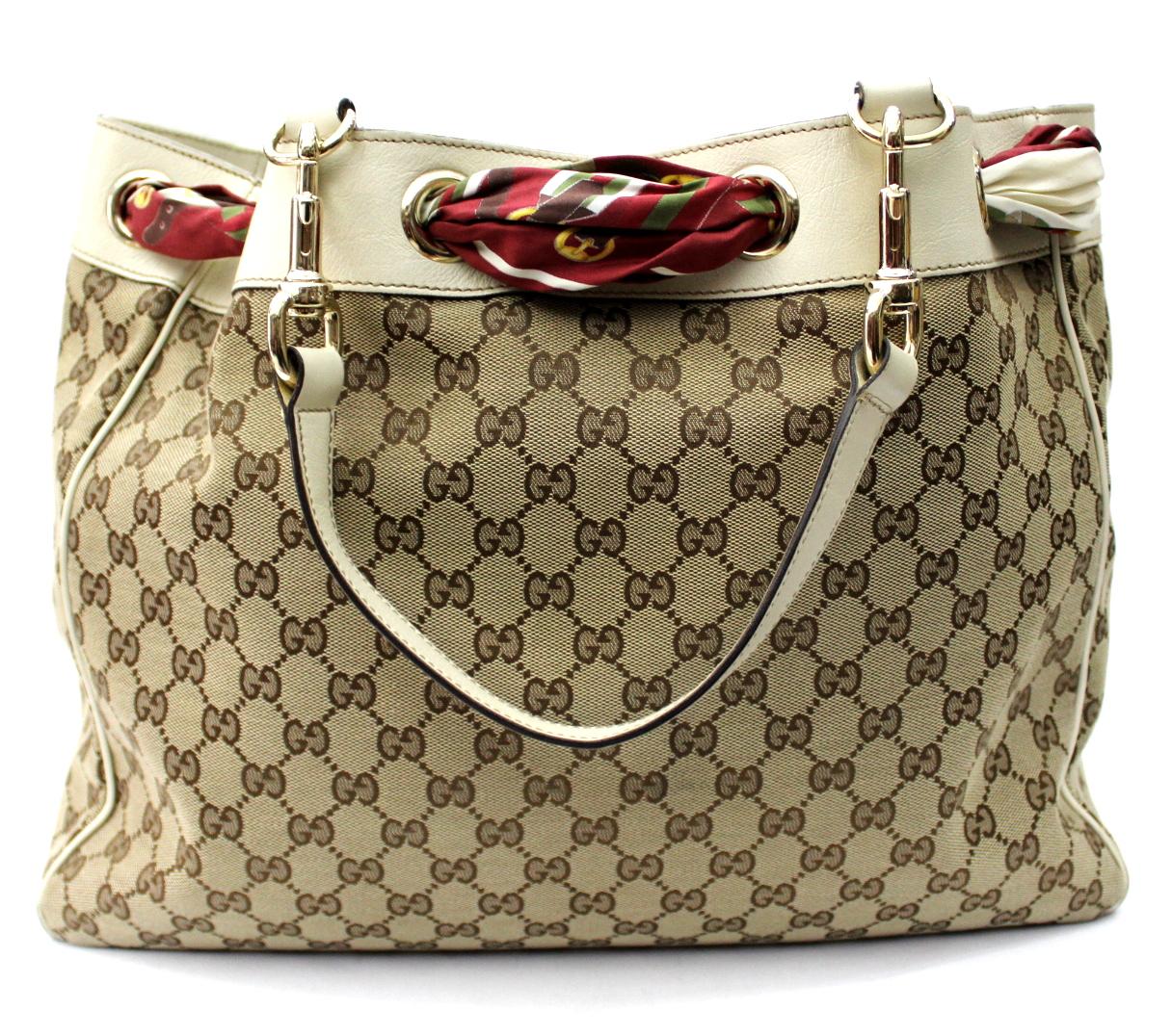 Don't miss out your opportunity to own this chic Gucci Beige GG Canvas Positano Bag. This popular style features durable GG fabric with a red Gucci silk scarf interlaced at the top. Its roomy interior is perfect for holding all your daily essentials
