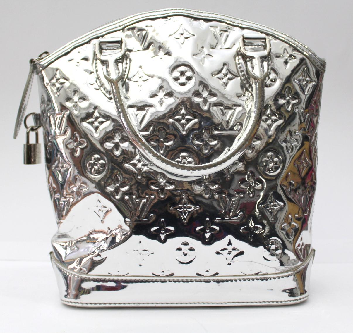 This Louis Vuitton Limited Edition Silver Monogram Miroir Lockit bag is a gorgeous and glamorous bag. This rare piece is made of ultra glossy monogrammed mirrored vinyl with patent leather trim and a lock to lock your precious objects. A definite