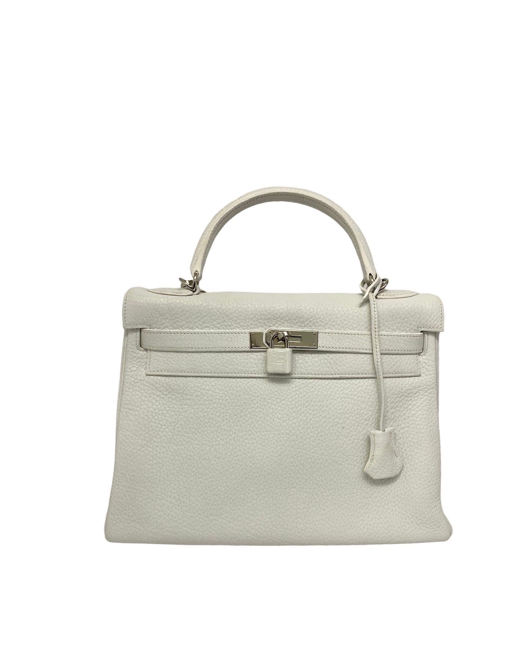 Hermès designer bag model Kelly 32 made of white textured leather with silver hardware.
Equipped with top handle and removable leather shoulder strap. Particular is the padlocks also covered in leather. Although the bag is white, it is presented in