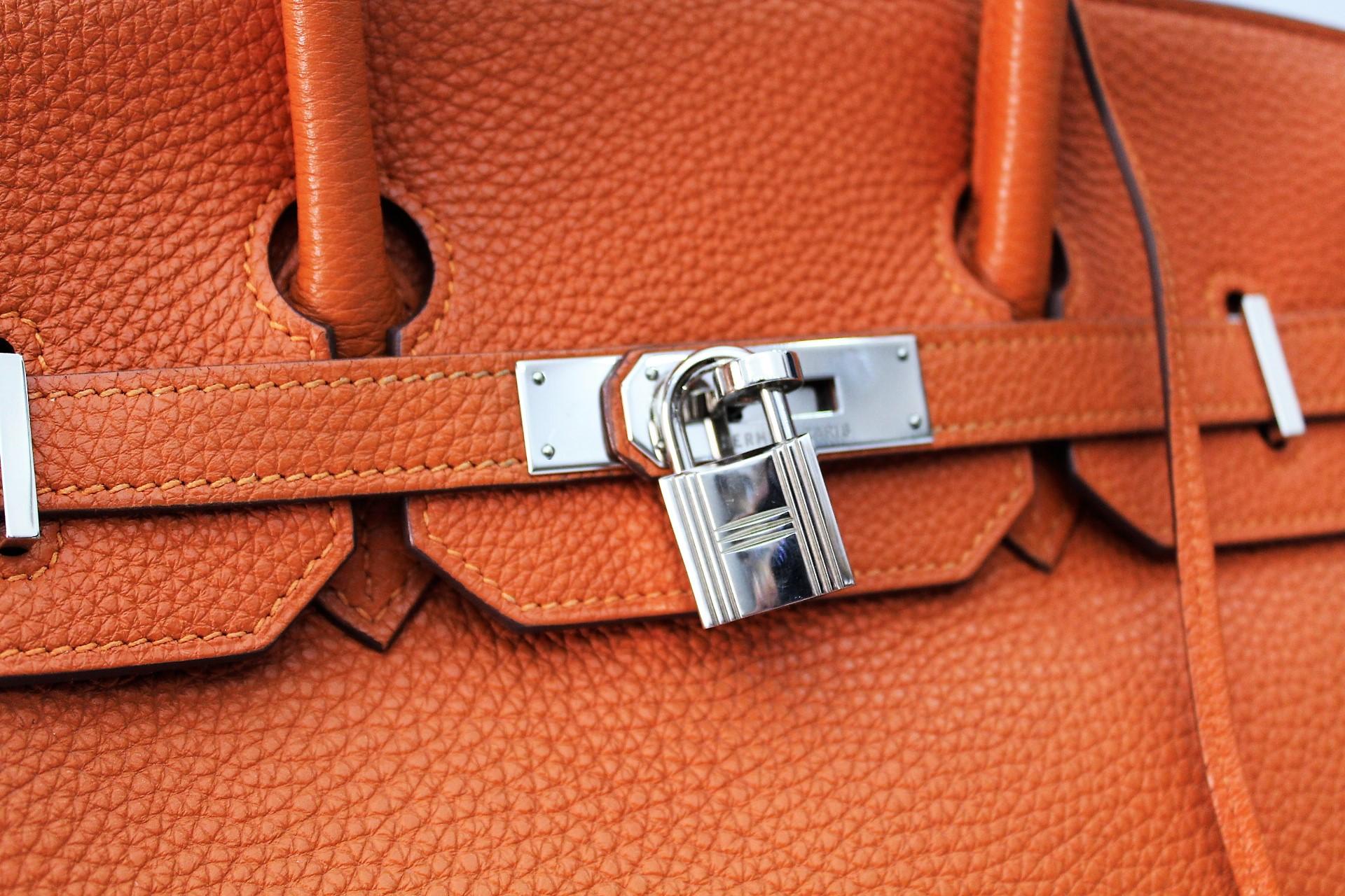 This elegant Birkin bag is made of Togo calf leather elaborately worked in orange. The bag features leather handles, a crossed flap with strap closure and a revolving palladium padlock, lock and a hanging clochette with keys. These open onto a