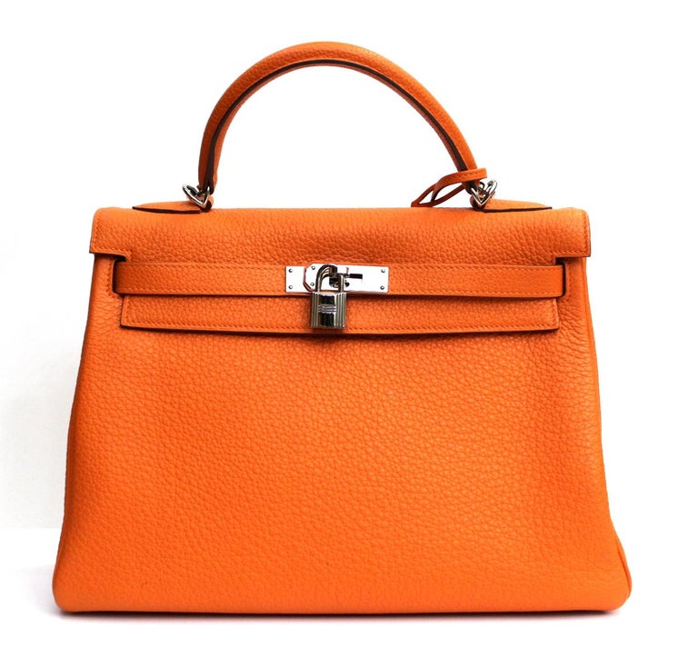 Fantastic Hermes Taurillon Clemence Kelly 32cm in orange leather. The bag features a leather-reinforced handle, silver hardware, an optional shoulder strap, a crossed flap and strap closure, a Kelly swivel latch, a lock and a bell hanging with the