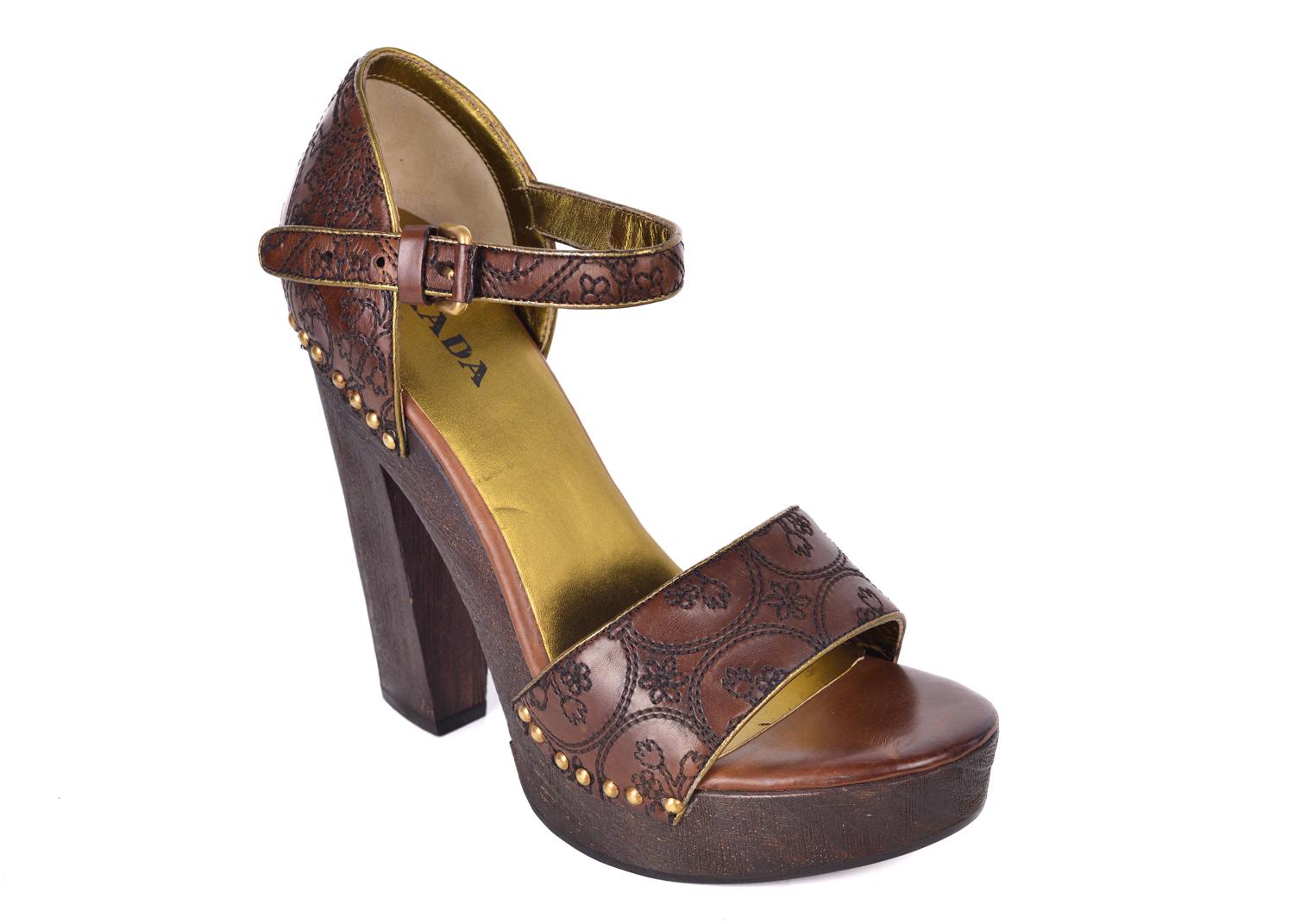 Rich brown leather pumps with a retro-chic aesthetic from Prada, courtesy of a skyscraper wooden block heel and platform.  Leather upper. Goldtone Rivets. Adjustable ankle strap. Leather lining. Rubber sole. Padded insole. platforms and buckle