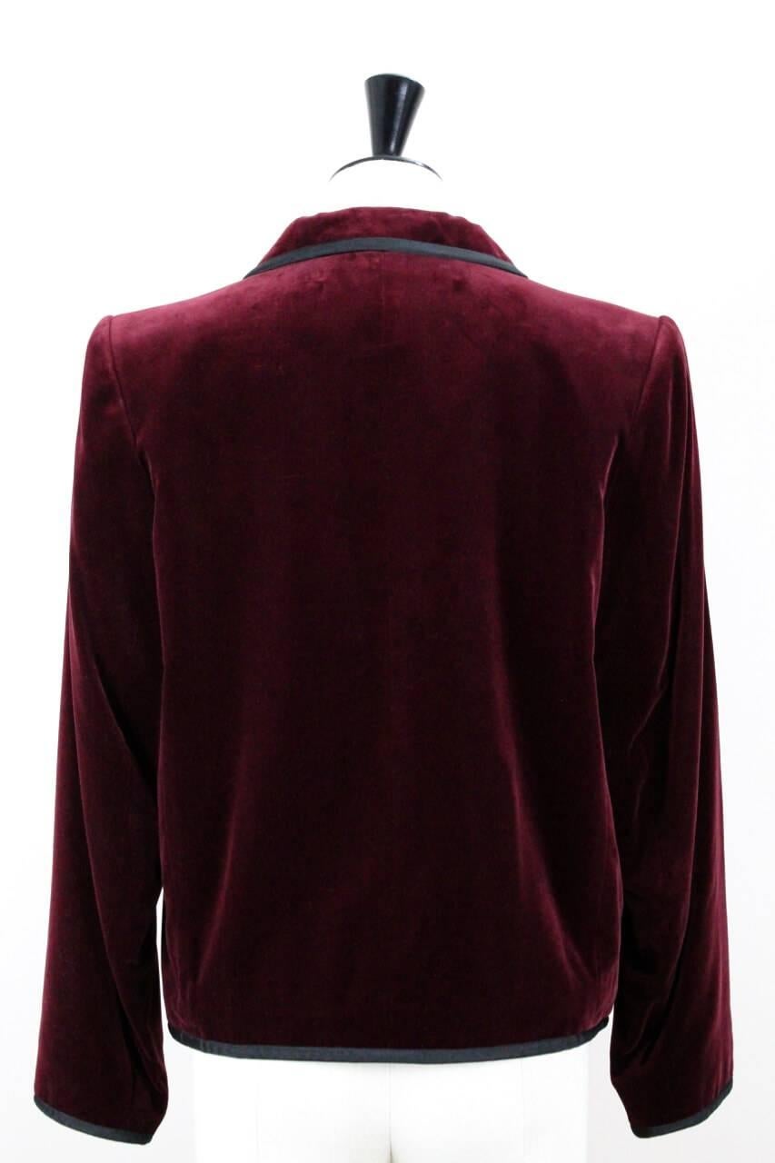 This Yves Saint Laurent straight cut deep burgundy cotton blend velvet blazer features a black textured ribbon trim detailing. It shows notched lapels, long sleeves, padded shoulders and two flap pockets on both sides. The blazer is fully lined in