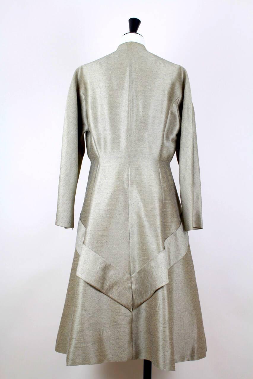 This sleek collarless coat is crafted from an amazing high quality coat weight taupe wool with a subtle sheen. It features bracelet length moderate dolman sleeves that close with a zip at the wrist, a fitted waist, a full skirt with a sewed on fish