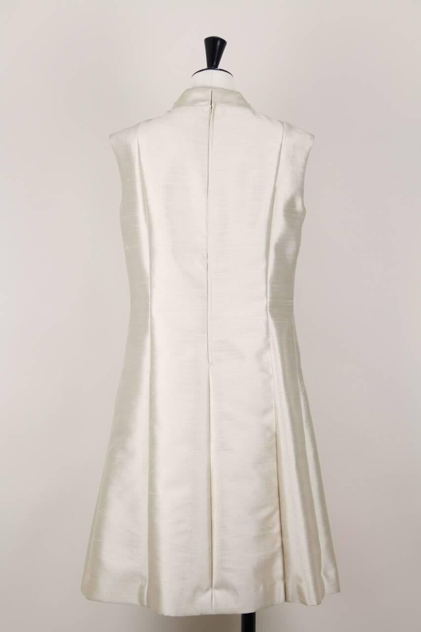 This sleeveless shift dress is made from a rich champagne raw silk. It features a simple architectural cut, an A-line silhouette with flattering princess seams and a small stand-up collar that is doubled on the front and embellished with two