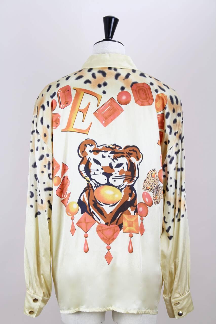 This 1991 documented loose-fitting signature Escada light gold blouse is made from shimmering soft silk and features a decorative animal and large gem print in orange hues, black and brown. It has long sleeves with buttoned cuffs, small shoulder