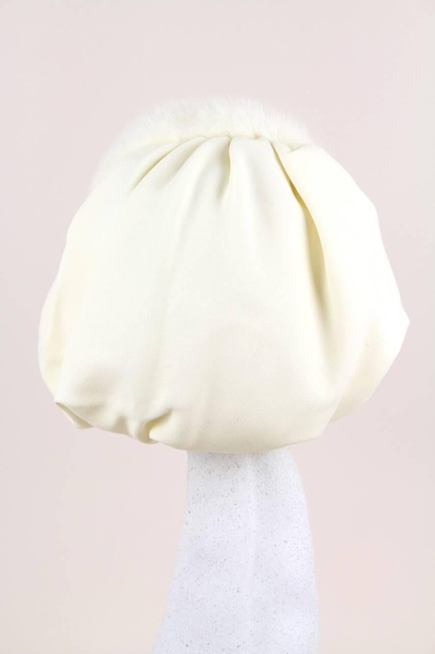 This rare and unusual bonnet-style hat is entirely made by hand of a cream fabric that feels like a silk crepe and soft and supple real mink fur of the same colour. It comprises of a stiffened mink fur covered headband hat and a soft sewed on ruched