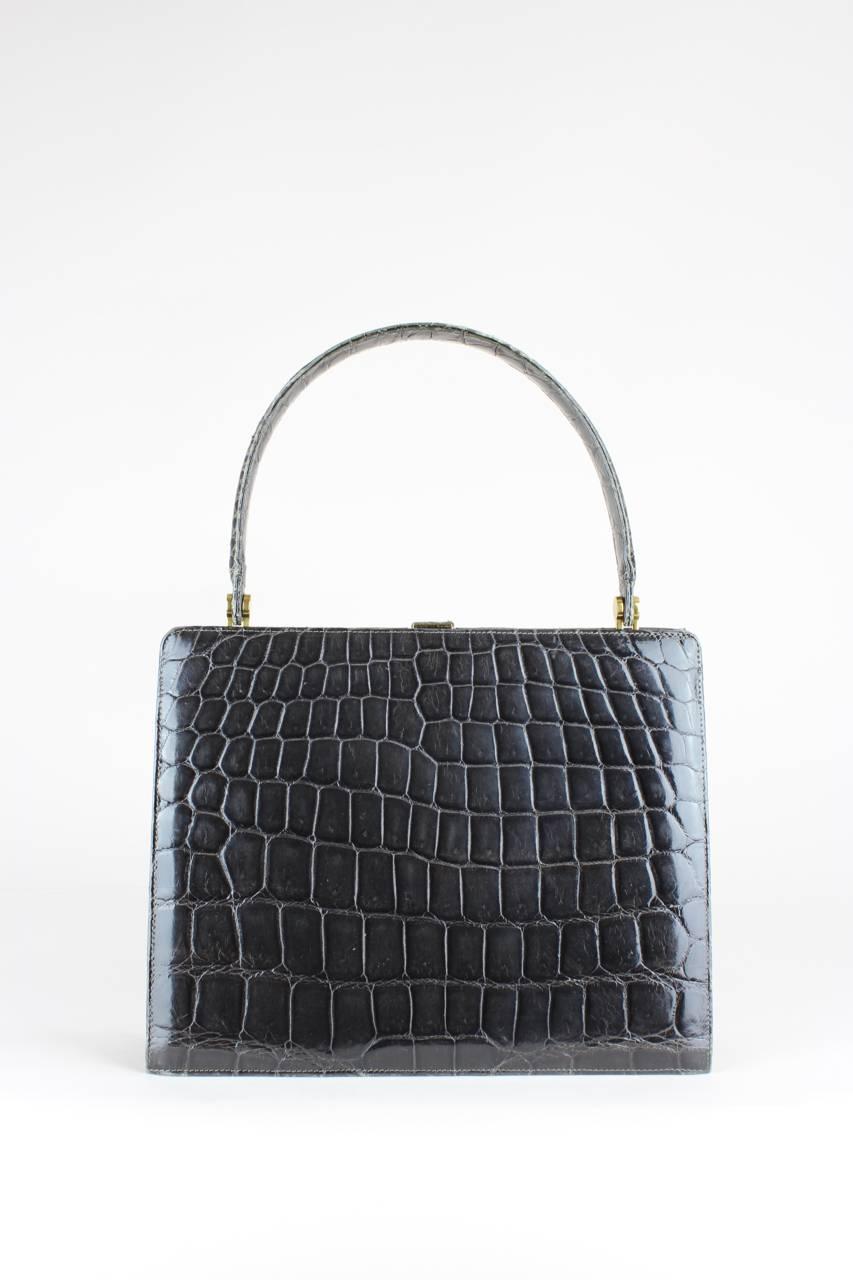 This crocodile print leather top handle bag shows a beautiful colour gradient from light grey (matt central panel) to charcoal grey (glossy sides) on the front whereas the glossy back is monochrome in dark grey. It has a rectangular shape, a