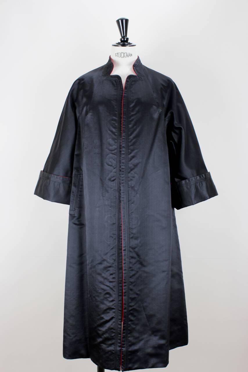 This low sheen satin fabric (silk or silk blend) evening coat is two coats in one. The bright red side features a tonal Japanese-inspired floral jacquard pattern and embroidery. The reverse side is all black. The coat shows a mandarin collar,