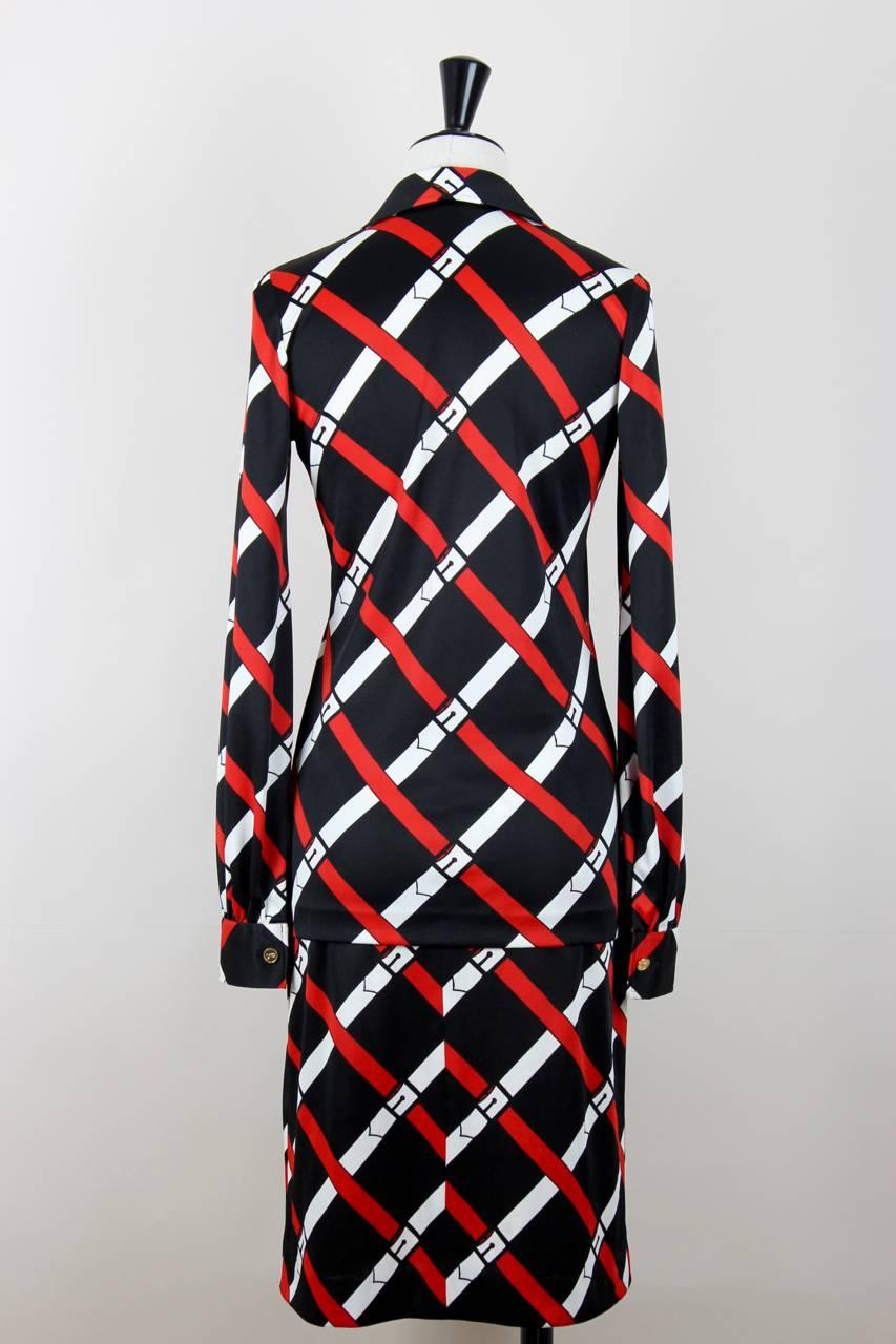 Este conjunto de blusa y falda de jersey presenta el característico estampado en trampantojo del cinturón en rojo y blanco sobre fondo negro, con la emblemática 