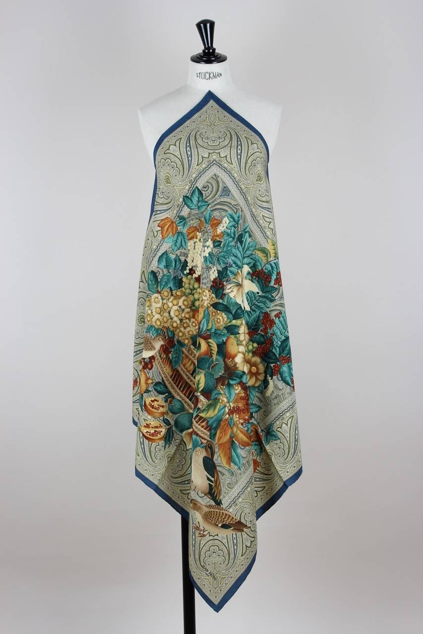 This autumn-coloured square scarf features a flower and fruit bouquet in a basket composed with some birds. It is bordered by a paisely pattern and a teal border. The scarf is made from silk, has a hand rolled-hem and is signed 