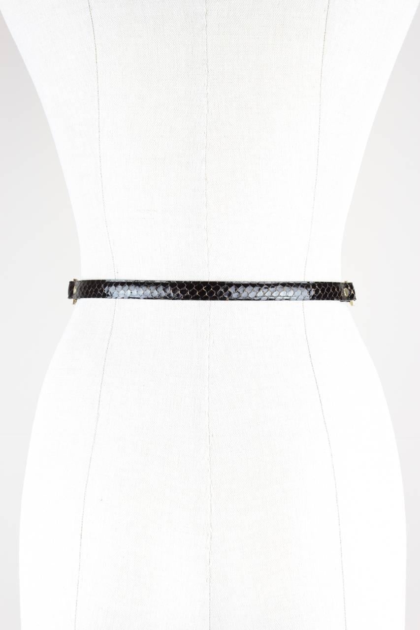 This classy wisp-thin belt is crafted from dark brown snakeskin leather. It features a gold-toned rectangular loop and hook buckle with cut out details and a gold-toned chain and stirrup embellishment on both sides.
 
Excellent vintage
