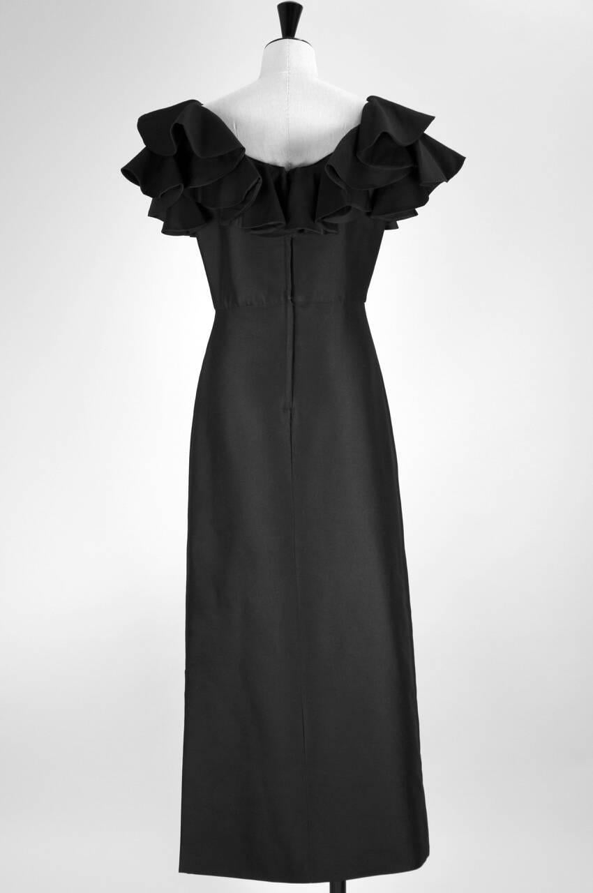 This gown is made from black wool and cotton mix fabric, probably rayon and is fully lined. The scooped neckline shows dramatic ruffles. The gown is fitted over the bust and waist. A 36 cm - 14.2