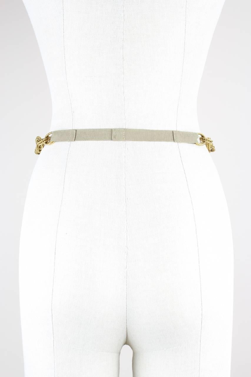 This adjustable belt features a gold-tone metal DG logo clasp in rose design, twisted metal chain links, a metal tassel and a khaki grosgrain ribbon in the back. It fastens by a hook and is signed 