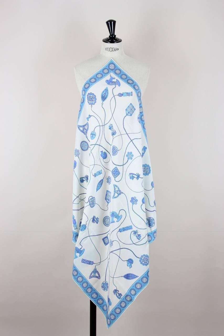 This crêpe de Chine silk scarf features an African design print with chains and pendants in azure and lavender on a creme-white background. It has a hand-rolled hem, its original label and care tag and shows the "Emilio" signature