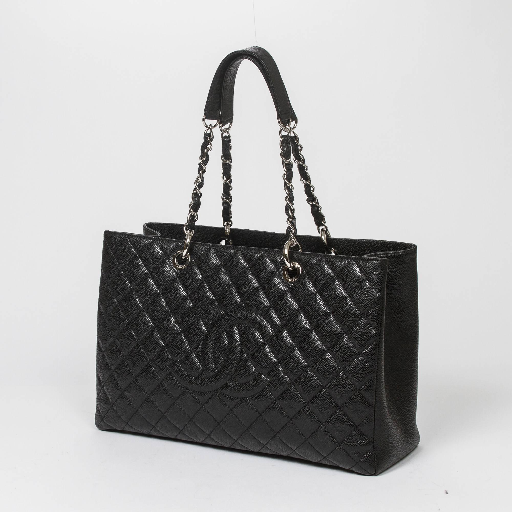 Grand Shopping Tote XL in black quilted caviar leather with chain and leather straps, silver tone hardware. Back slip pocket. 4 protective metal feet at the base. Black satin lined interior with one zipped middle compartment, 2 slip pockets and one