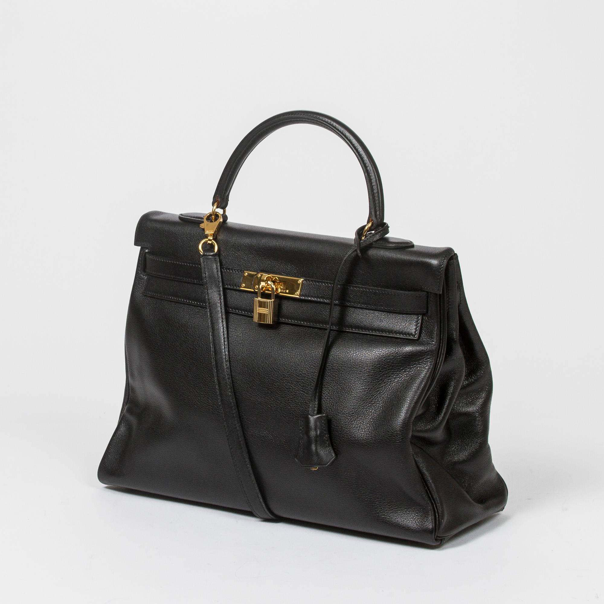 Kelly Retourne 35 in black Evergrain leather with optional strap, cadenas and keys in clochette, gold tone hardware. Interior lined in black chèvre leather with 2 slip pockets and one zip pocket. Stamp A in square. Model from 1997. Dustbag included.