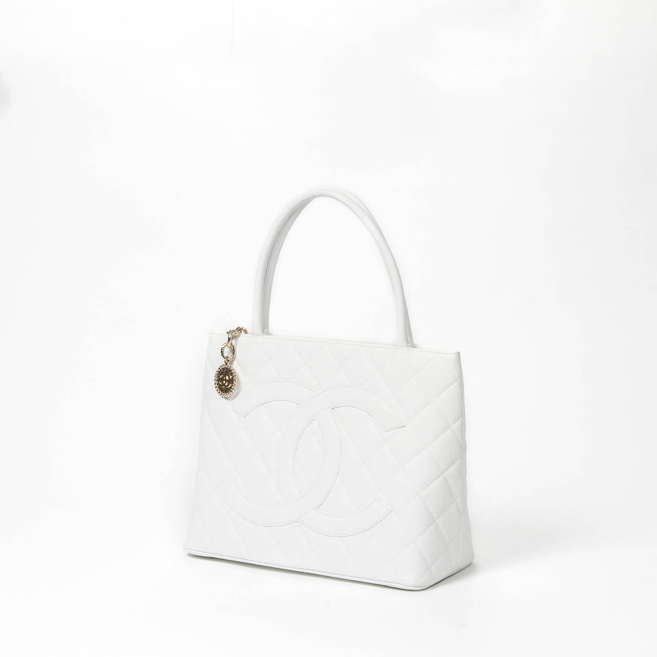 Médaillon in white grained quilted leather with back slip pocket and gold tone hardware. White leather lined interior with one slip and one zip pocket, authenticity sticker included. Model of 2002 (code : 7255325) . Box and dustbag included.