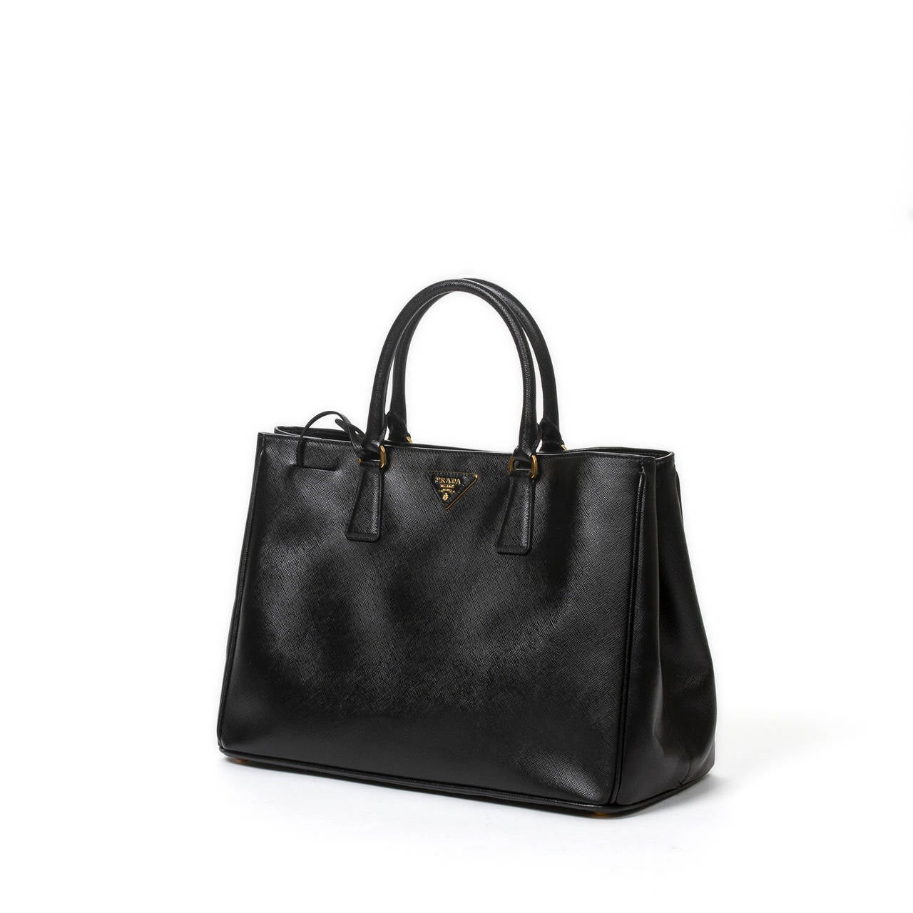 Prada Saffiano Lux handbag in black grained leather with key ring in clochette, gold tone hardware. Black jacquard canvas lining with 3 slip pockets and one zip pocket. Dustbag included. Very slight crease on leather, perfect condition.