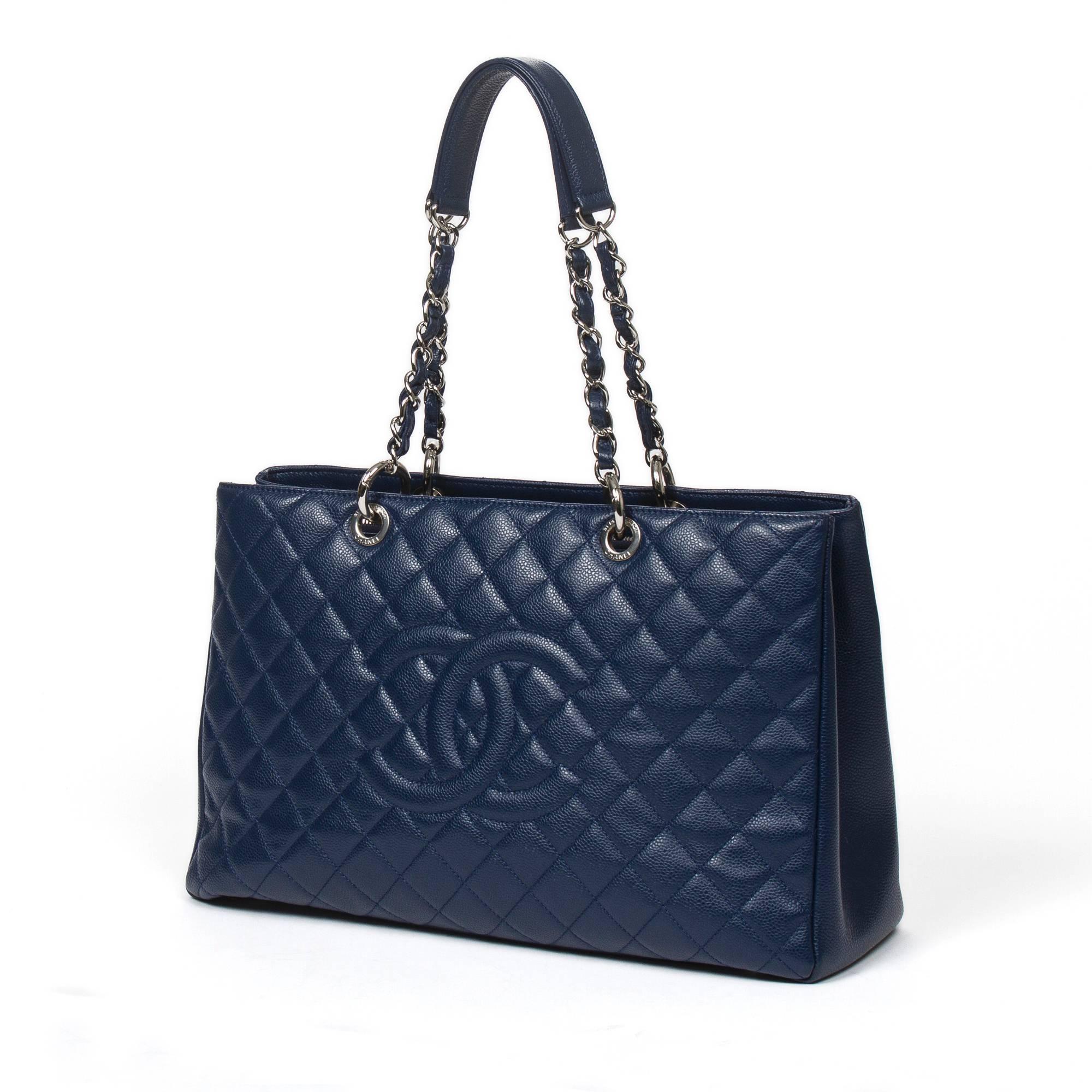 Grand Tote Shopping XL in navy blue quilted caviar leather with chain and leather straps, silver tone hardware. Back slip pocket. 4 protective metal feet at the base. Grey satin lined interior with one zipped middle compartment, 2 slip pockets and