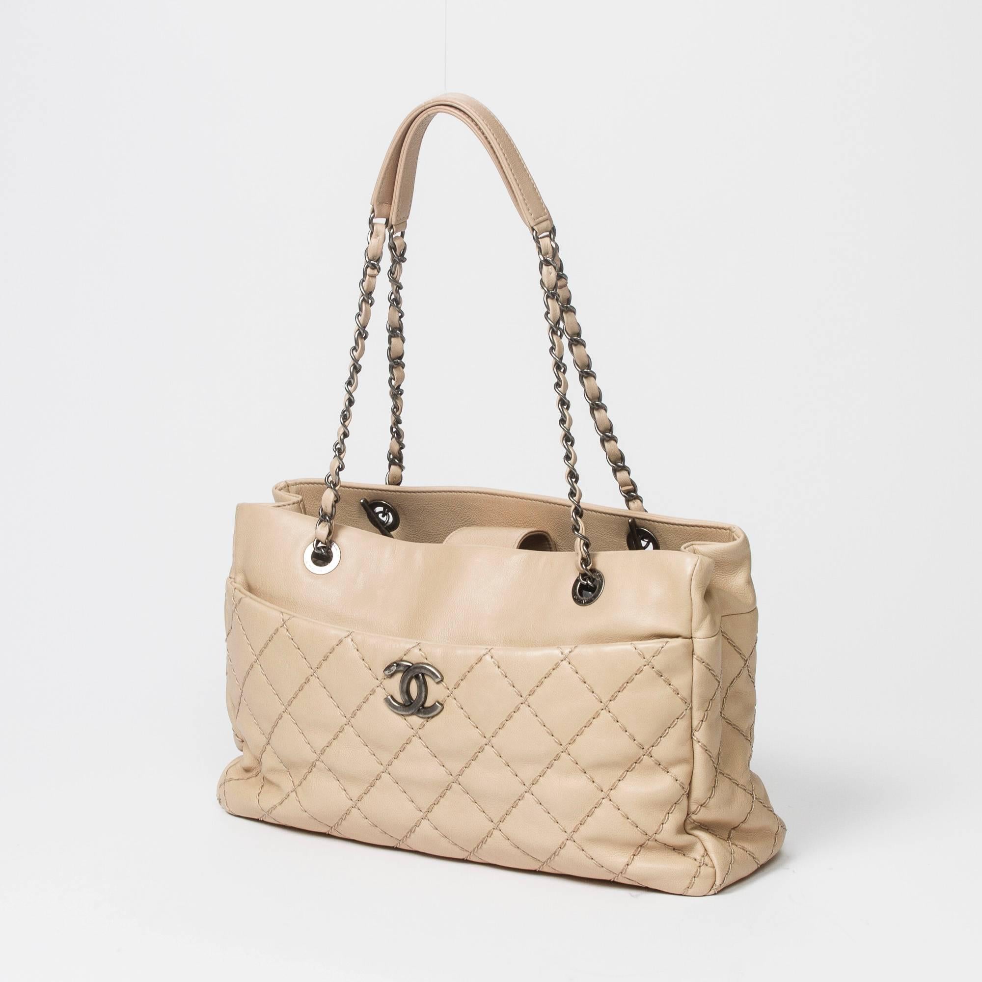 Tote in beige stitch quilted leather with antique silver tone hardware. CC front pocket with magnetic closure. 4 protective feet. Magnetic closure. 2 compartment bag with grey fabric lined interior, large zip middle comparment, 2 slip pockets and
