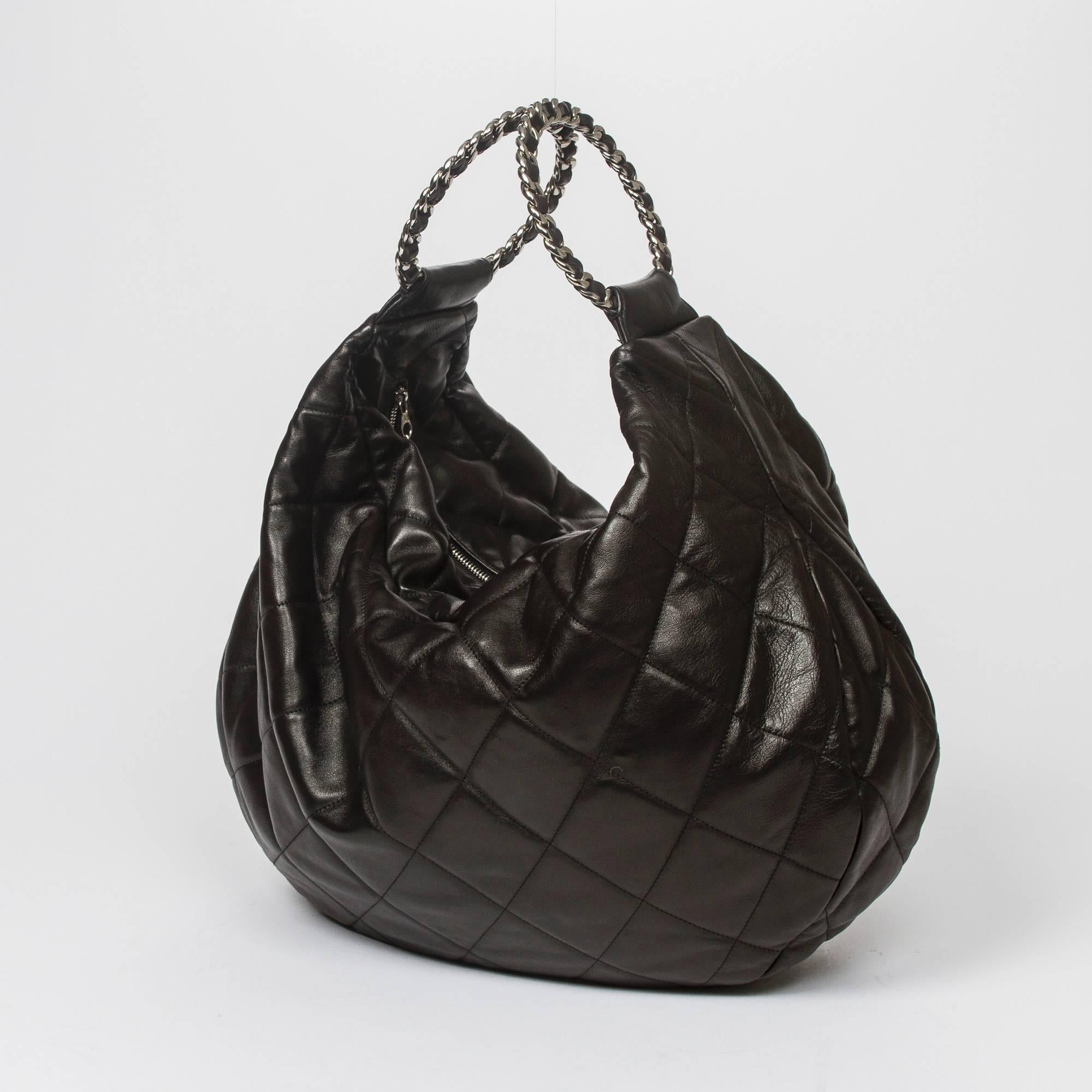 Hobo handbag in black quilted leather, 2 chain motif ring handles interlaced with leather, silver tone hardware. Zip closure. Black fabric lined interior with slip pocket and one zip pocket. Silver tone heat stamps 
