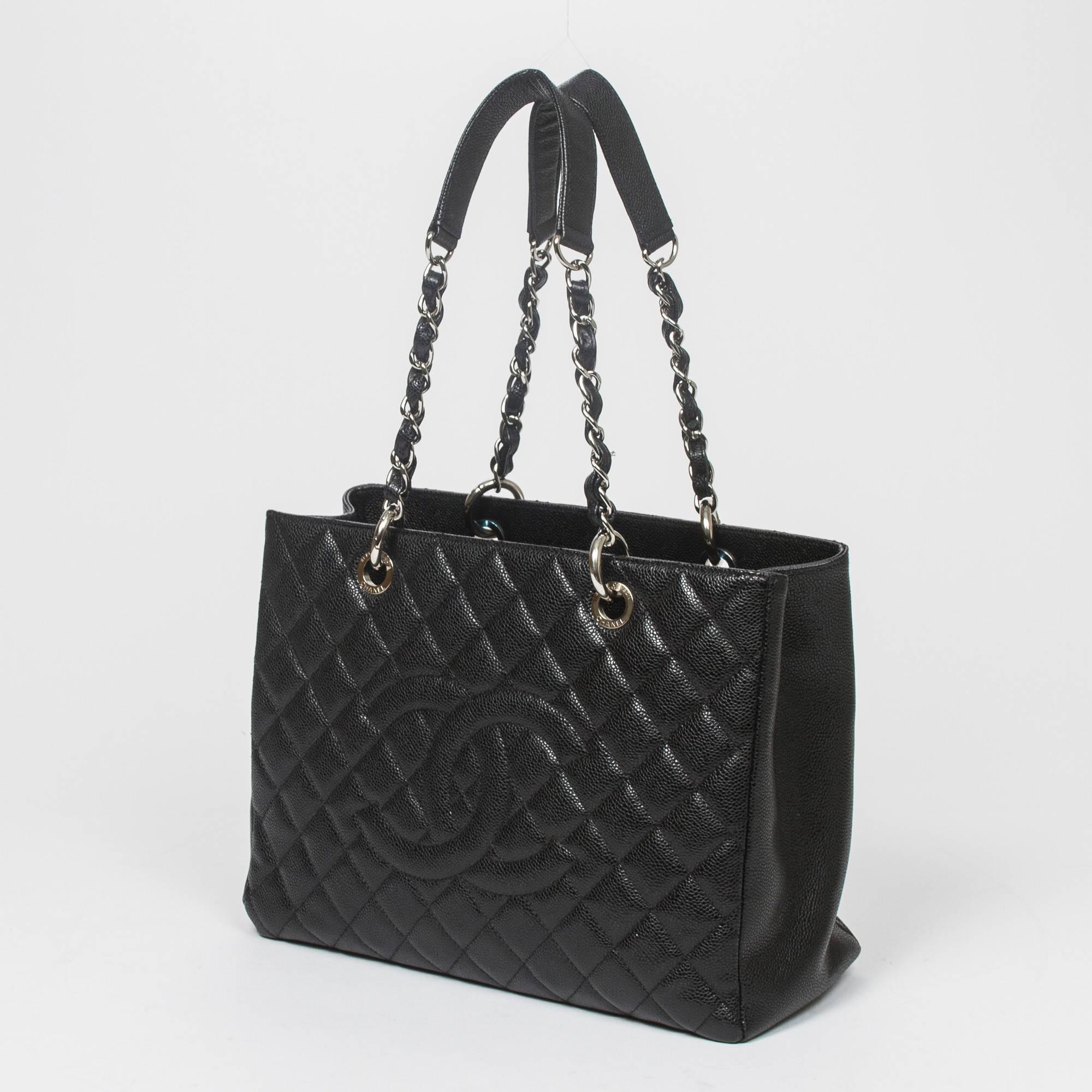 Grand Shopping Tote in black quilted caviar leather with chain and leather straps, silver tone hardware. Back slip pocket. Black satin lined interior with one zipped middle compartment, 2 slip pockets and one zip pocket. Silver tone heat stamp