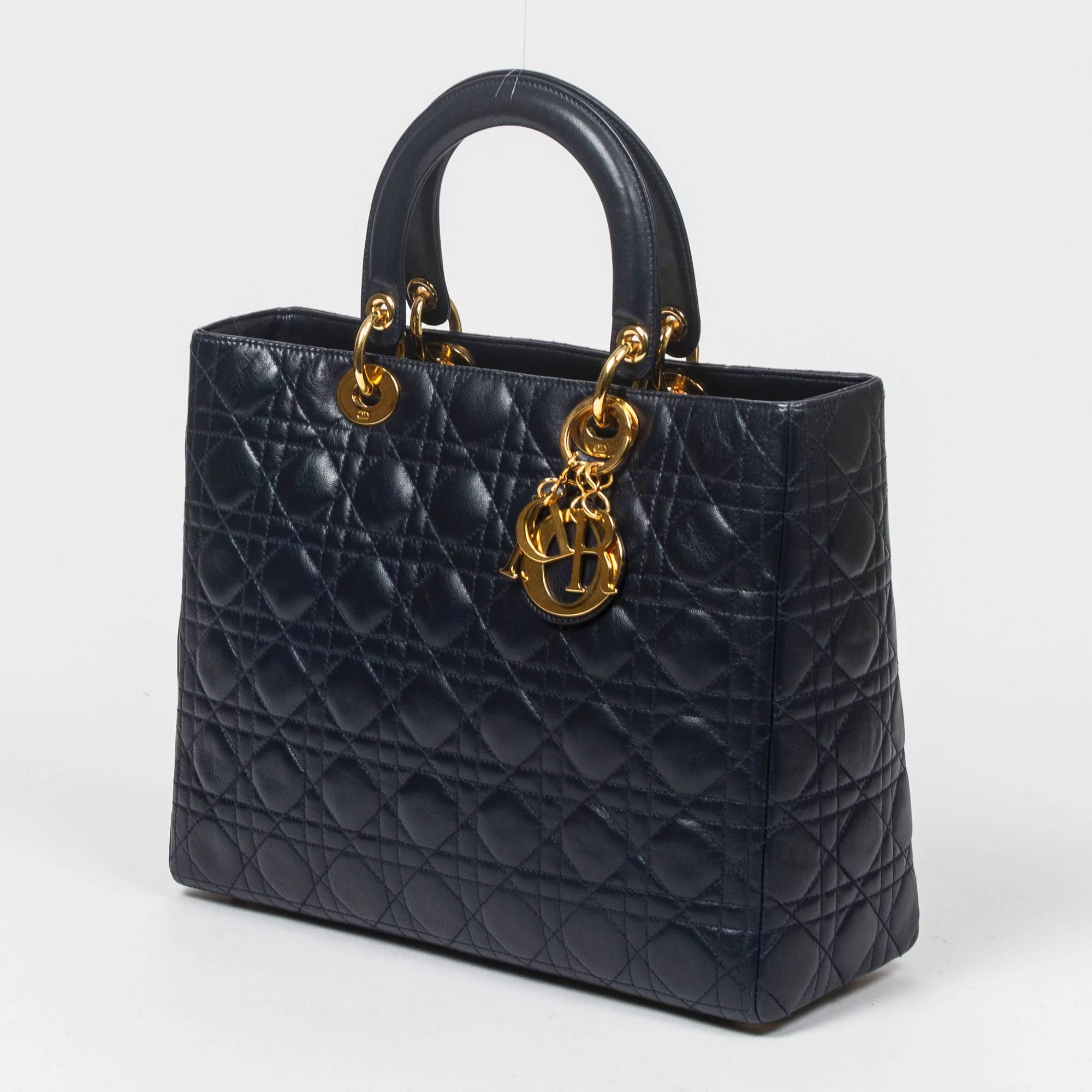 Lady Dior GM in navy blue cannage leather with optional shoulder strap and gold tone hardware. 5 protective feet. Zip closure. Red jacquard fabric lined interior with one zip pocket. Production number MA-0957. Model from 1997. There are some scuffs