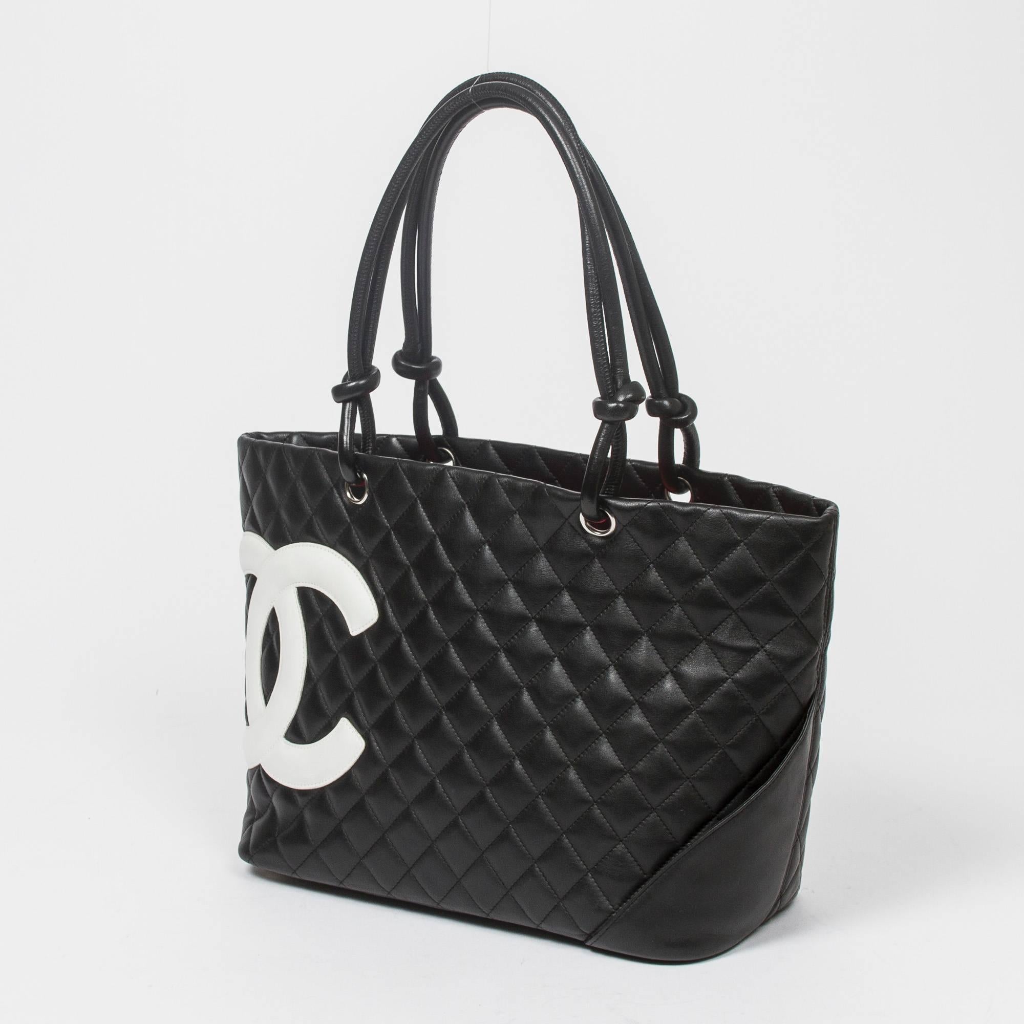 Cambon Tote GM in black quilted leather with white leather CC and silver tone hardware. Back slip pocket. 5 protective feet. Zip closure. Flashy pink jacquard canvas lined interior with one compartment, 2 zip pockets and lobster claw key ring.