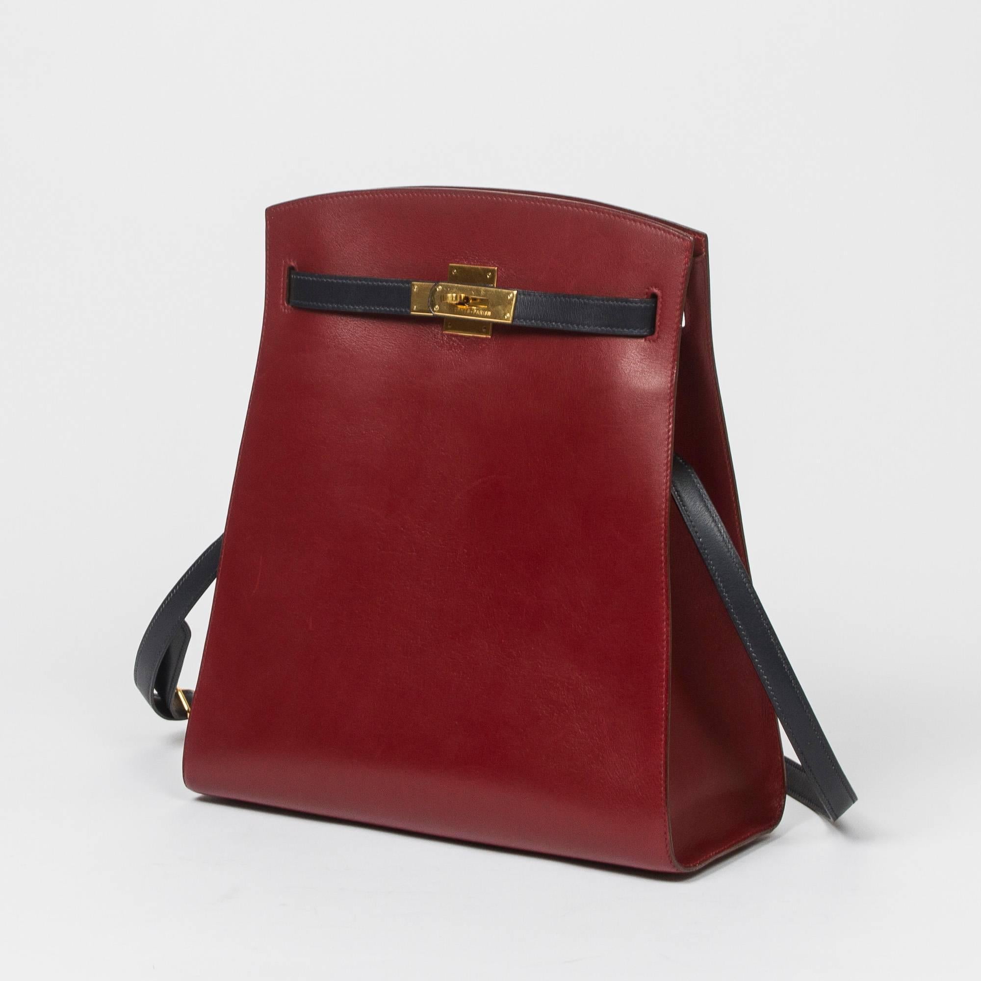 Kelly Sport GM Bicolor in Rouge H box leather with navy adjustable shoulder straps and closure straps, gold tone hardware. 4 gold tone protective feet. Interior lining in Rouge H in chèvre with one slip pocket and one zip pocket. Stamp V in a