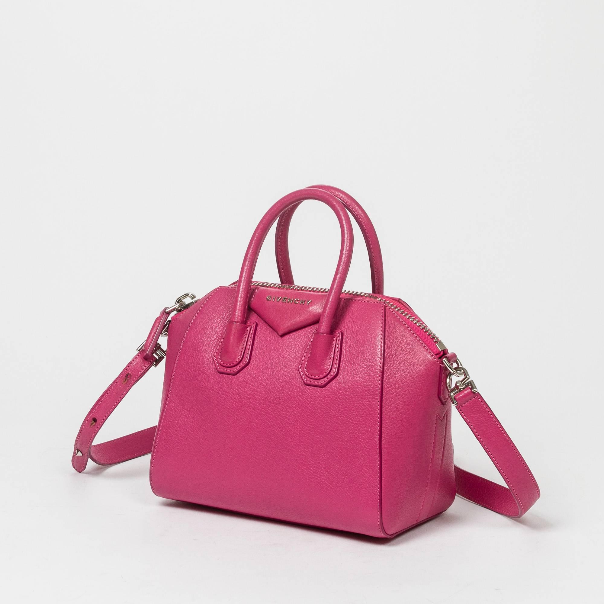 Antigona Mini in fuchsia grained leather with optional shoulder strap and silver tone hardware. Zip closure. Beige fabric lined interior with 2 slip pockets and one zip pocket. Production number 3C0114. Dustbag included. Very light signs of wear on