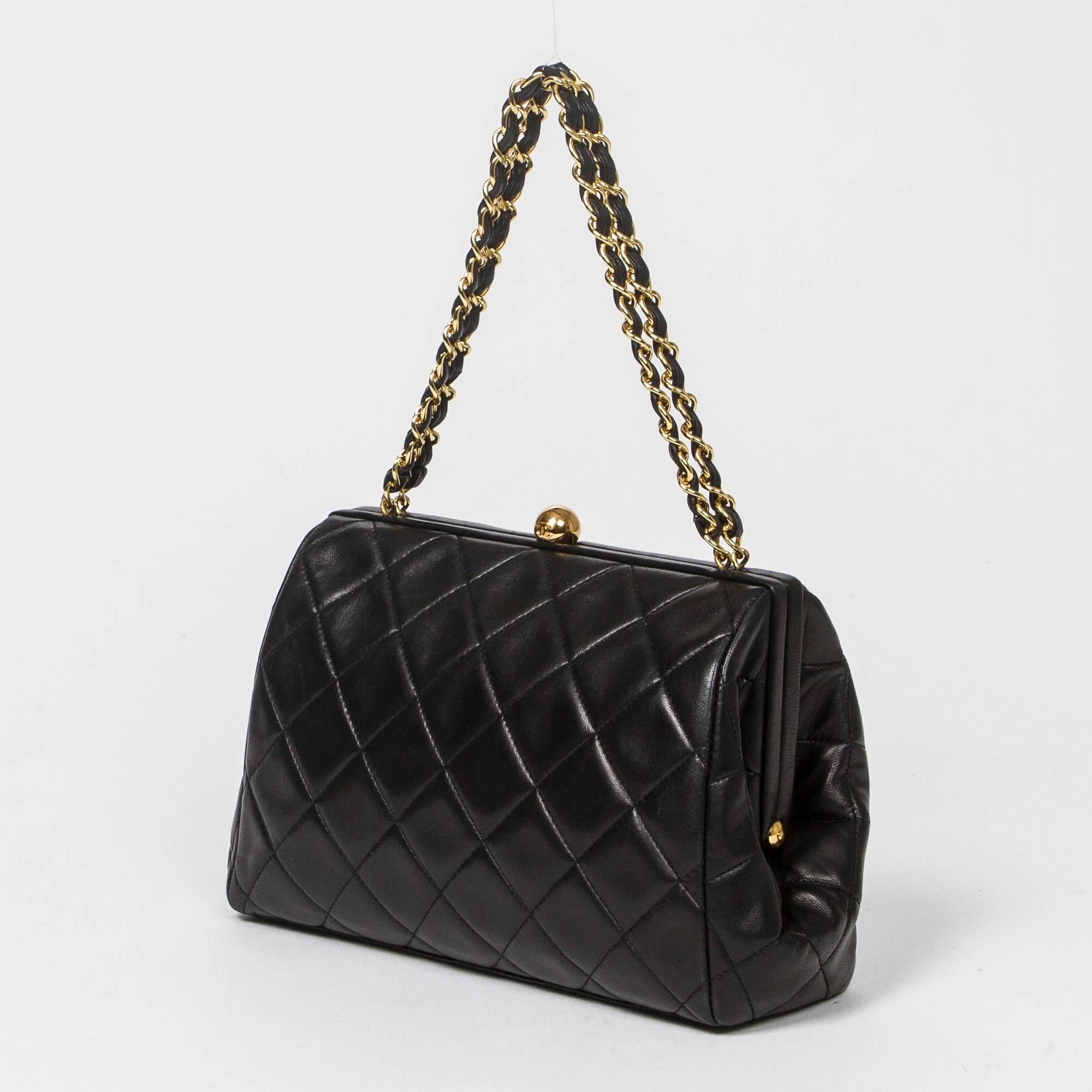 Vintage handbag in black quilted leather with gold tone chain strap interlaced with black leather. Kiss closure. Black leather interior with one zip pocket and a slip pocket. Heat gold stamp 