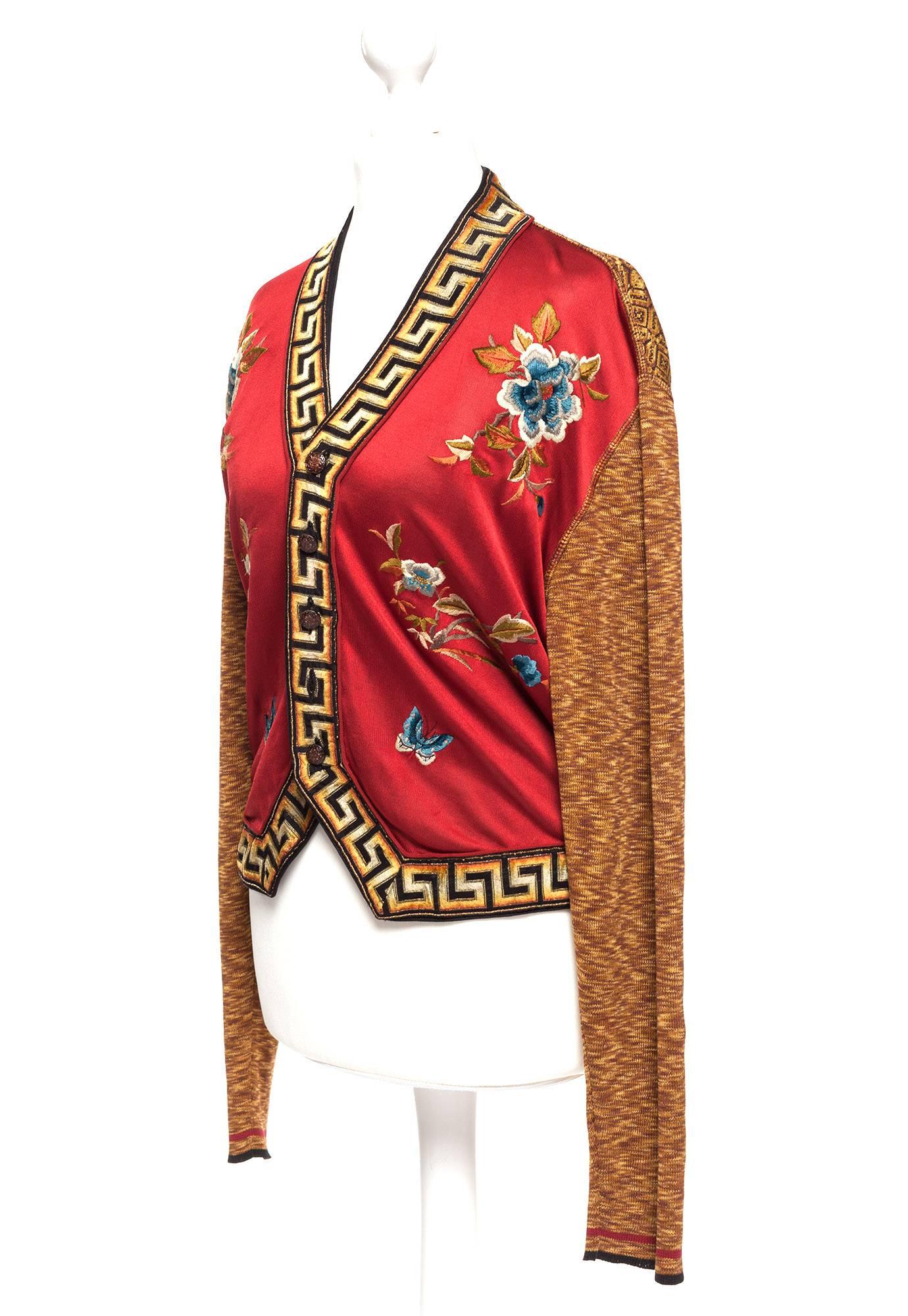  Cardigan is in a space dye gold tone knit, red satin front panels with multi colored flowers, black gold, red tone greek key trim around neck and bottom front with black and floral metal buttons, a true design classic from JPG.