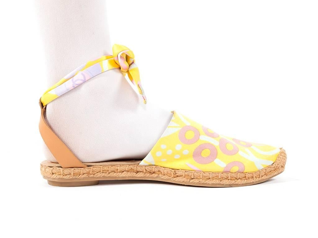 espadrilles have a cool abstract floral print in bright yellow with pastel blue and pinks. ankle strap is printed fabric and tan leather, rubber outer soles with small flat heel. 
