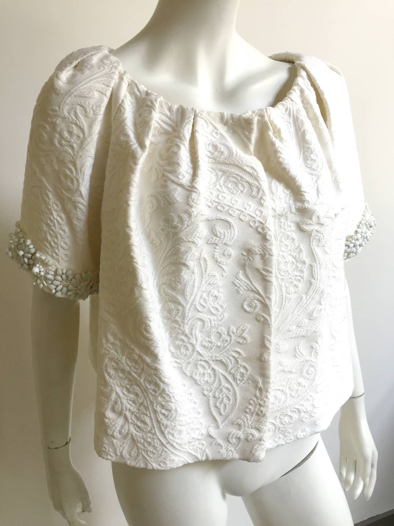 Giambattista Valli Paris white damask embellished open neck short sleeve jacket  size 10 / 44 and made in Italy.  There are 3 snap front buttons and jacket is lined. Gorgeous beaded sleeve trim adds that extra pizzazz.  
The height of jacket is 20