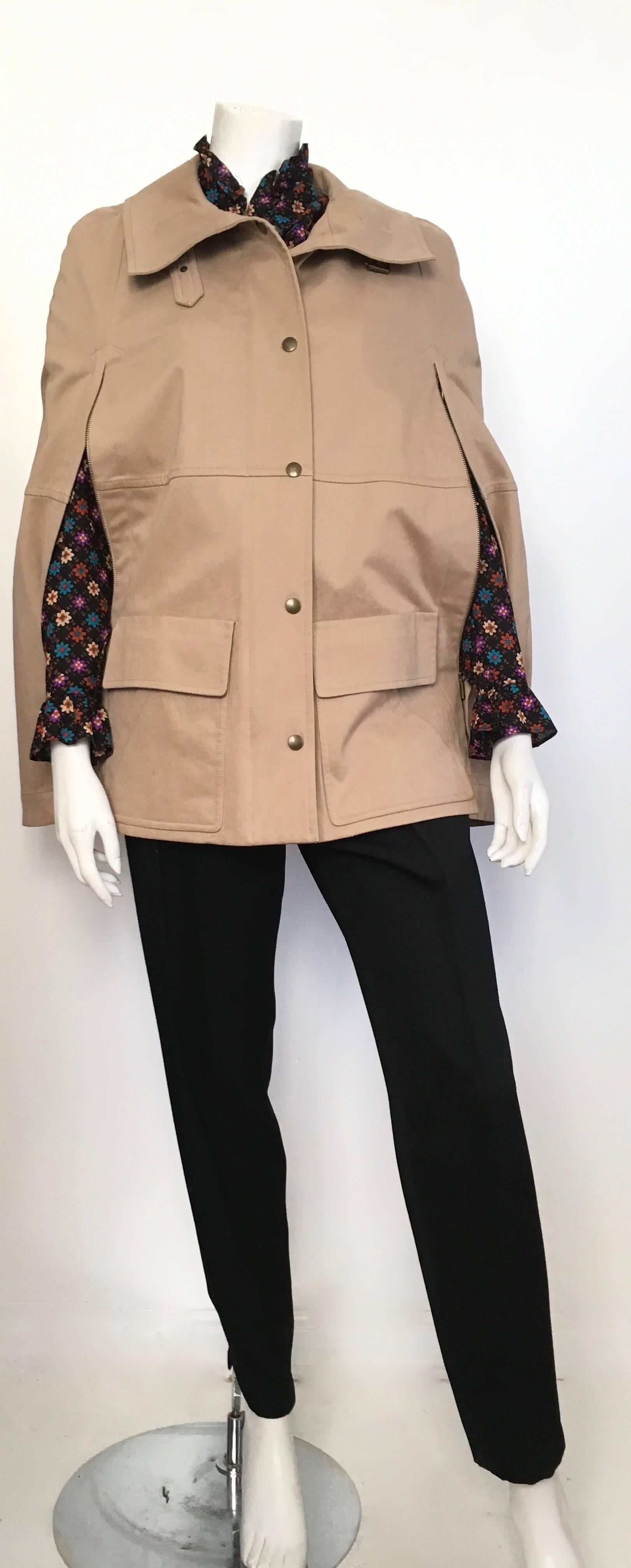 Akris punto khaki cotton snap button & zipper front safari cape size 6.  Both sides of cape has zipper to let your arms out.  There are pockets on front of cape. There is a buckle at collar that gives cape an extra touch of sophistication. Cape is