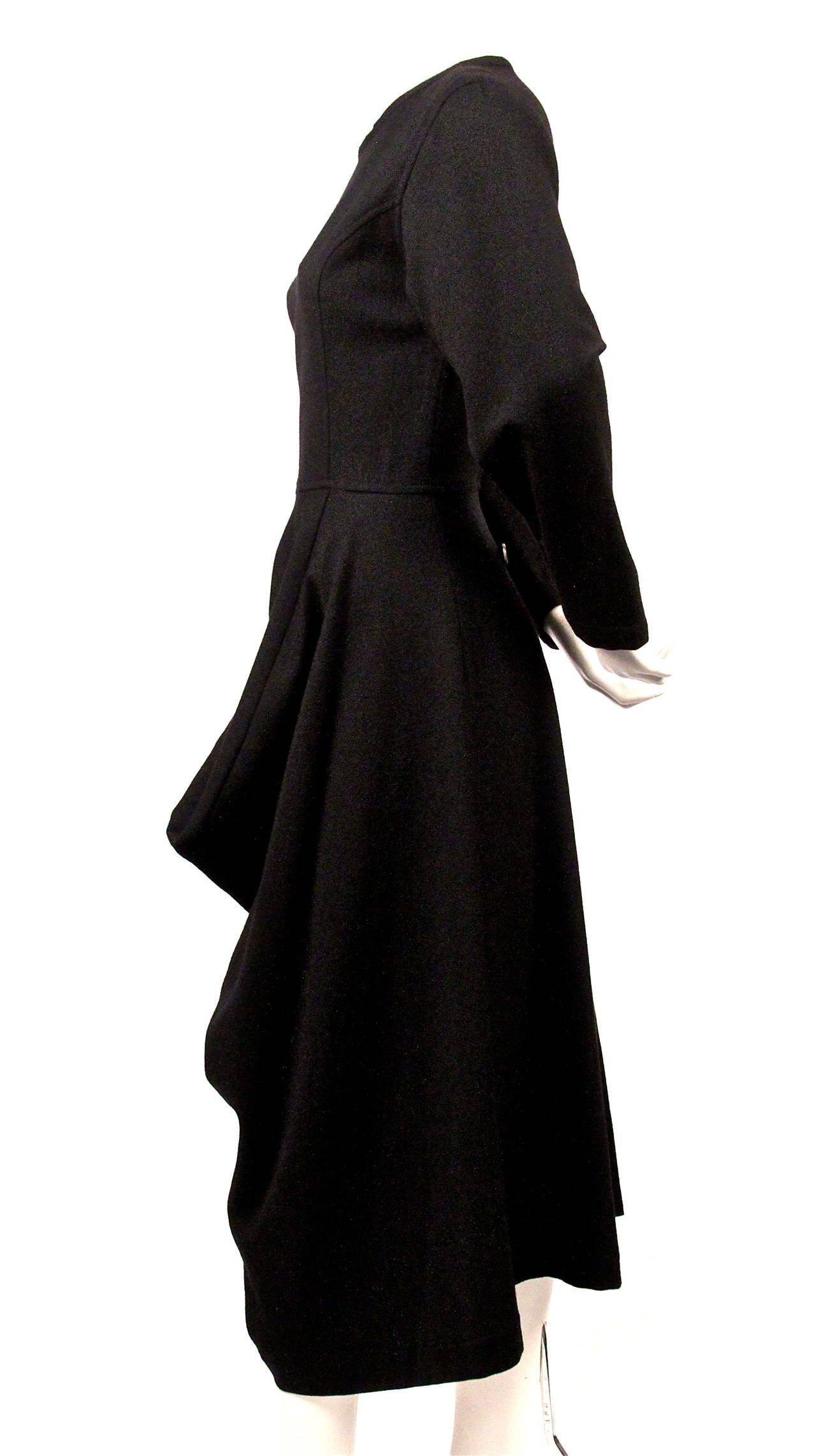 Jet black asymmetrically cut wool dress with draped panel from Comme des Garcons dating to fall of 1985. Dress is labeled a size 'S'. Approximate measurements: shoulders 16